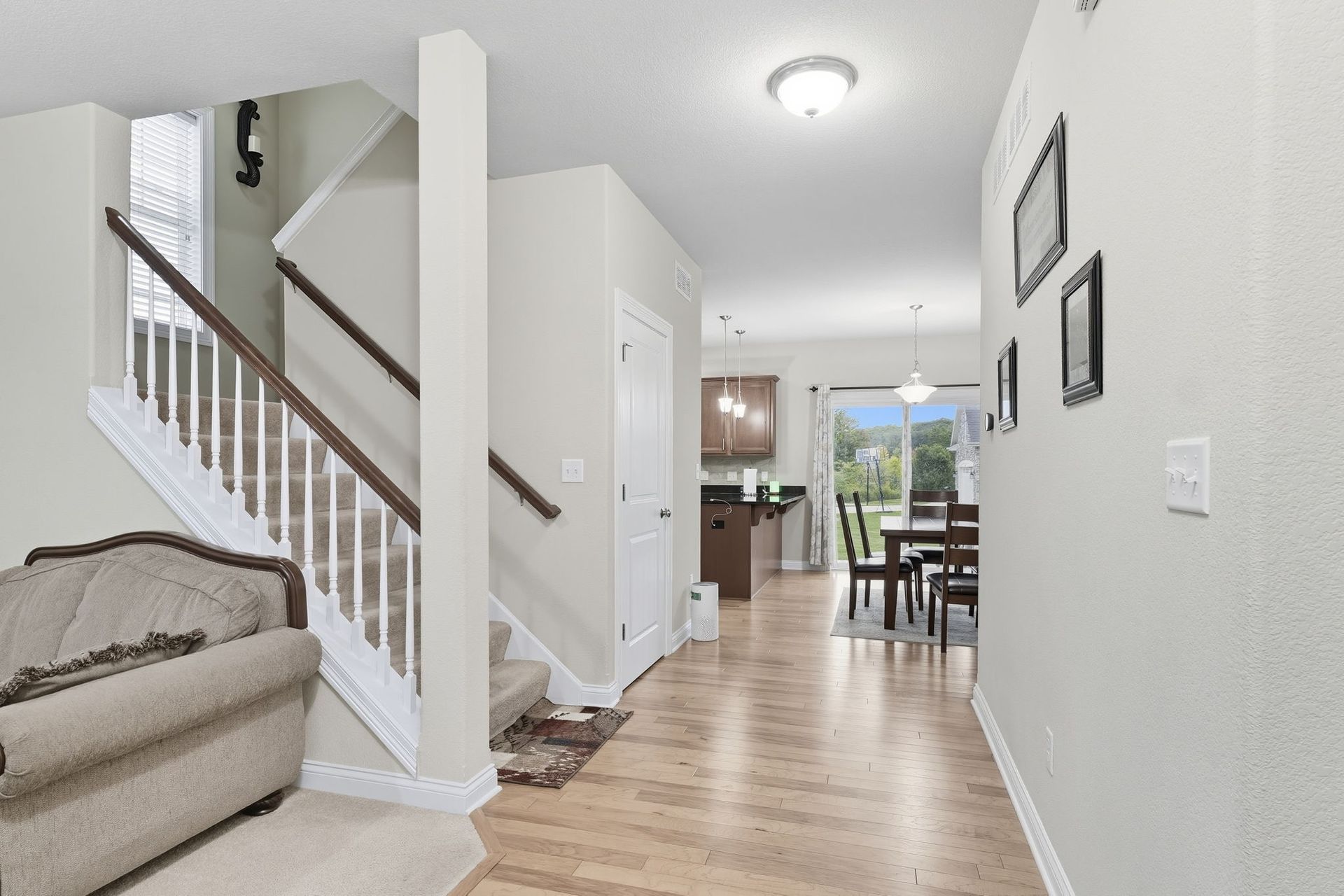 Bright hallway with wood floors, staircase, and a view into a kitchen and dining area
