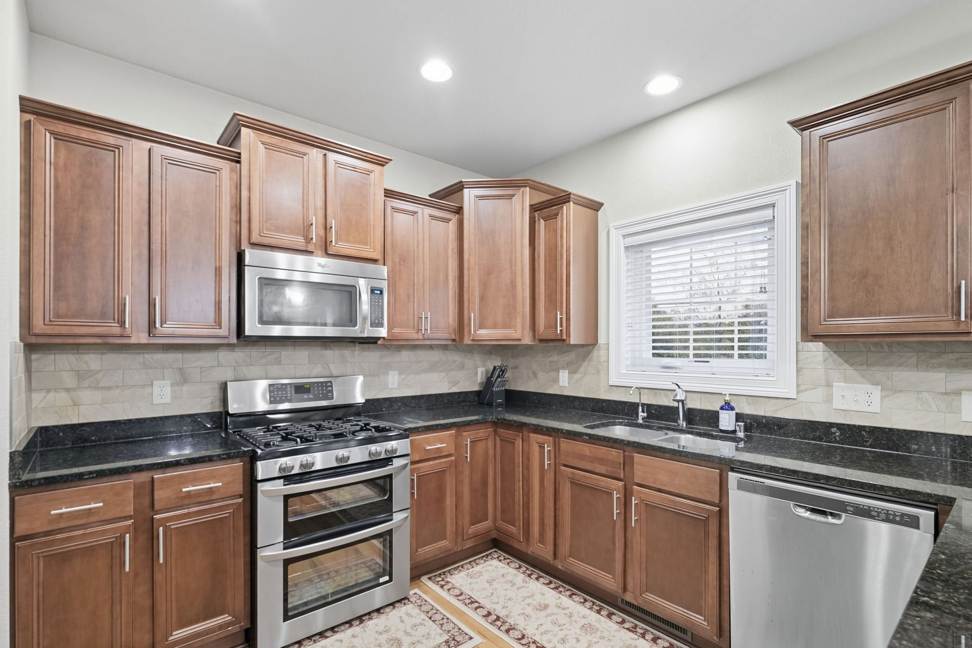 Modern kitchen with wood cabinets, black countertops, stainless appliances, and a window above the sink