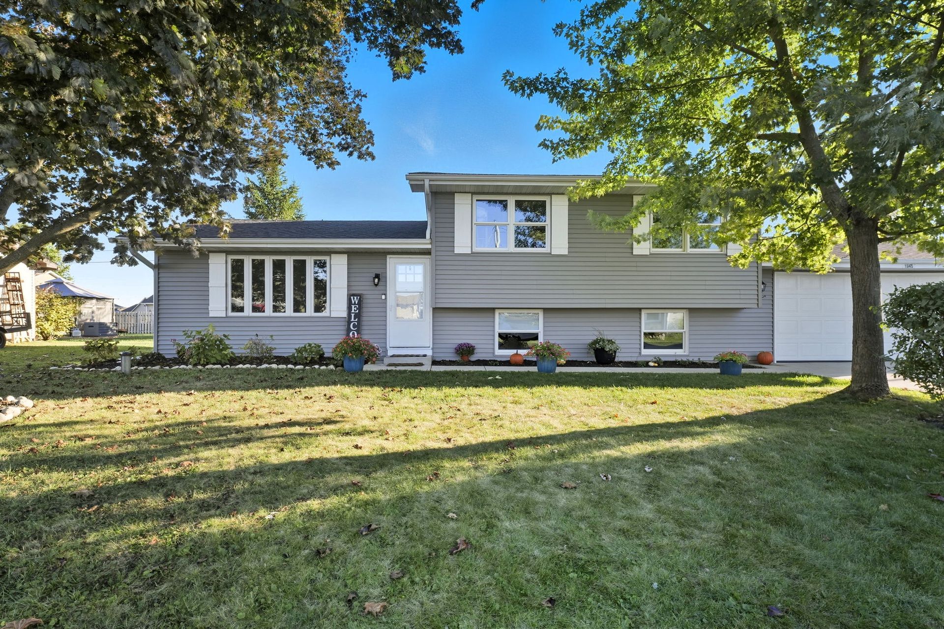 Suburban split-level house with gray siding, white trim, and a front lawn under a blue sky