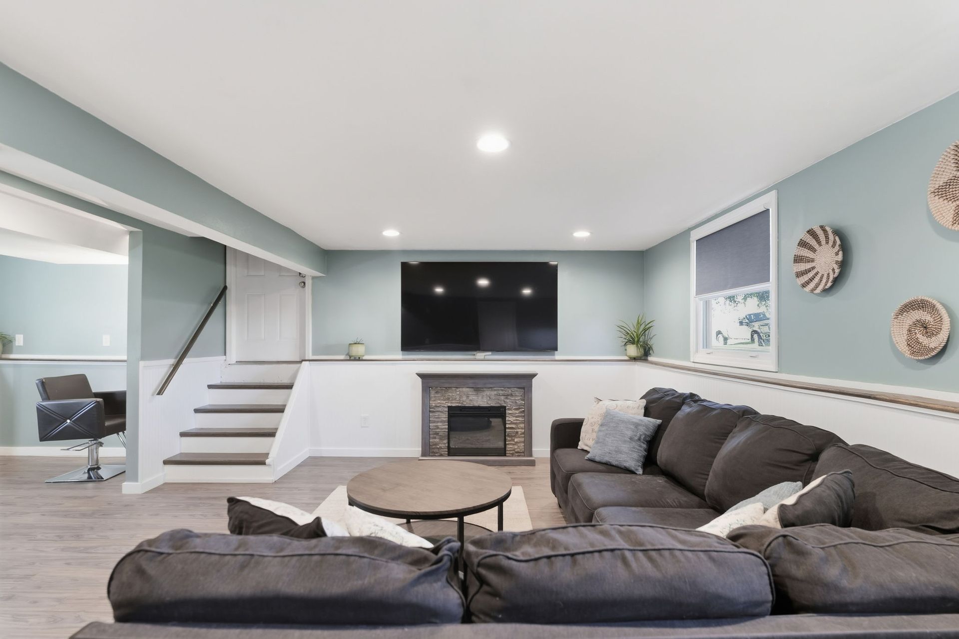 Bright living room with gray sectional, fireplace, stairs, and wall-mounted TV.