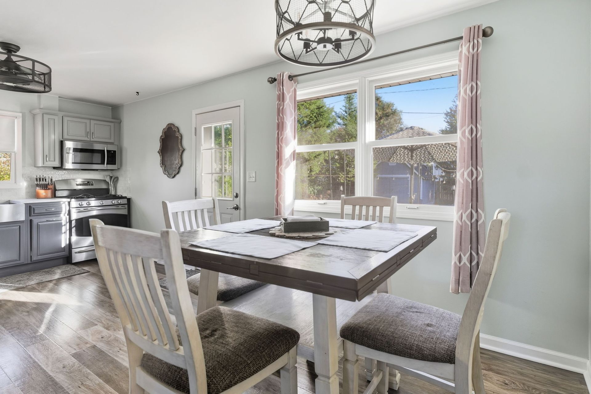 Bright dining room with a wooden table, gray chairs, and a kitchen visible in the background.