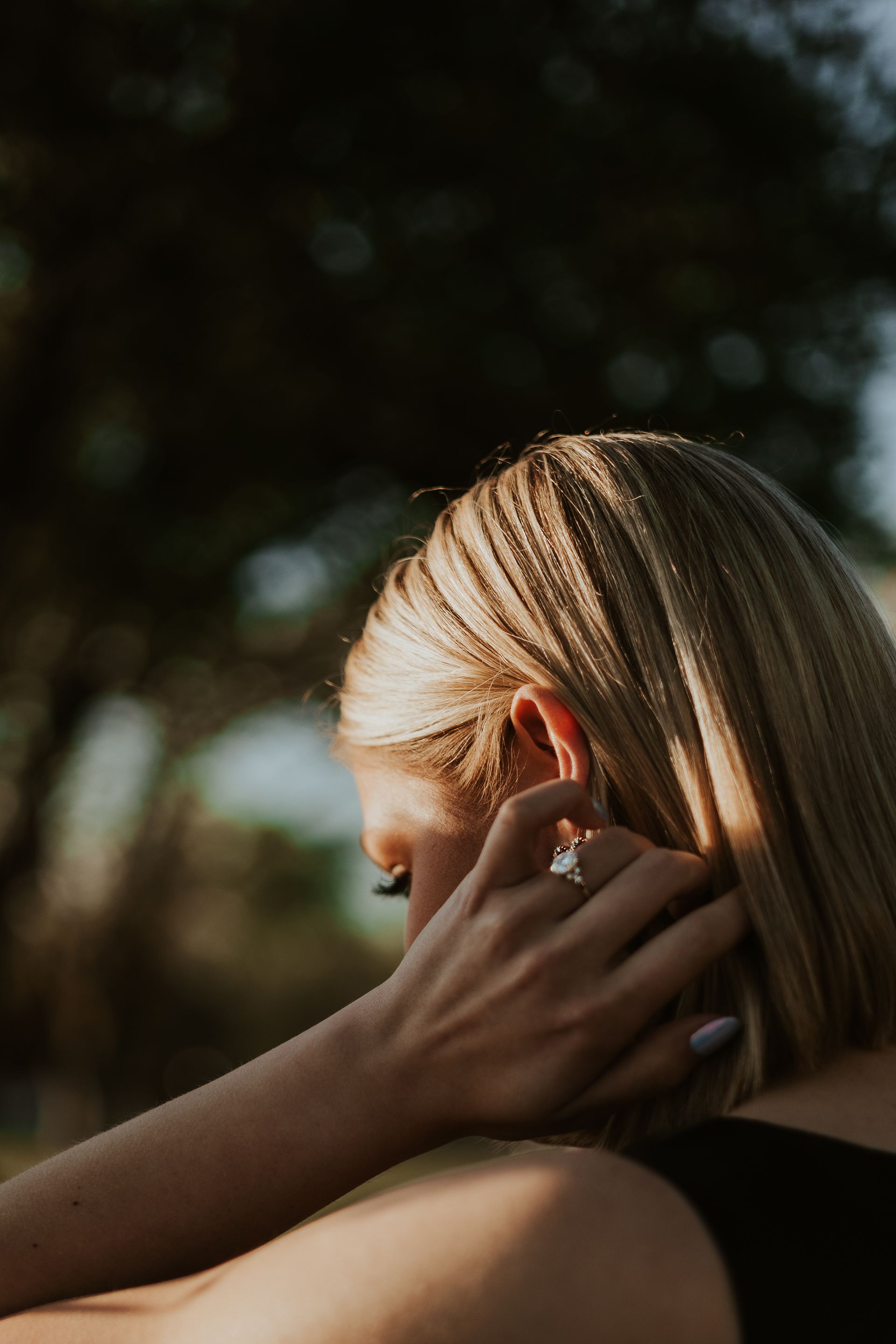 Person with short blonde hair touching their ear outdoors in soft sunlight.
