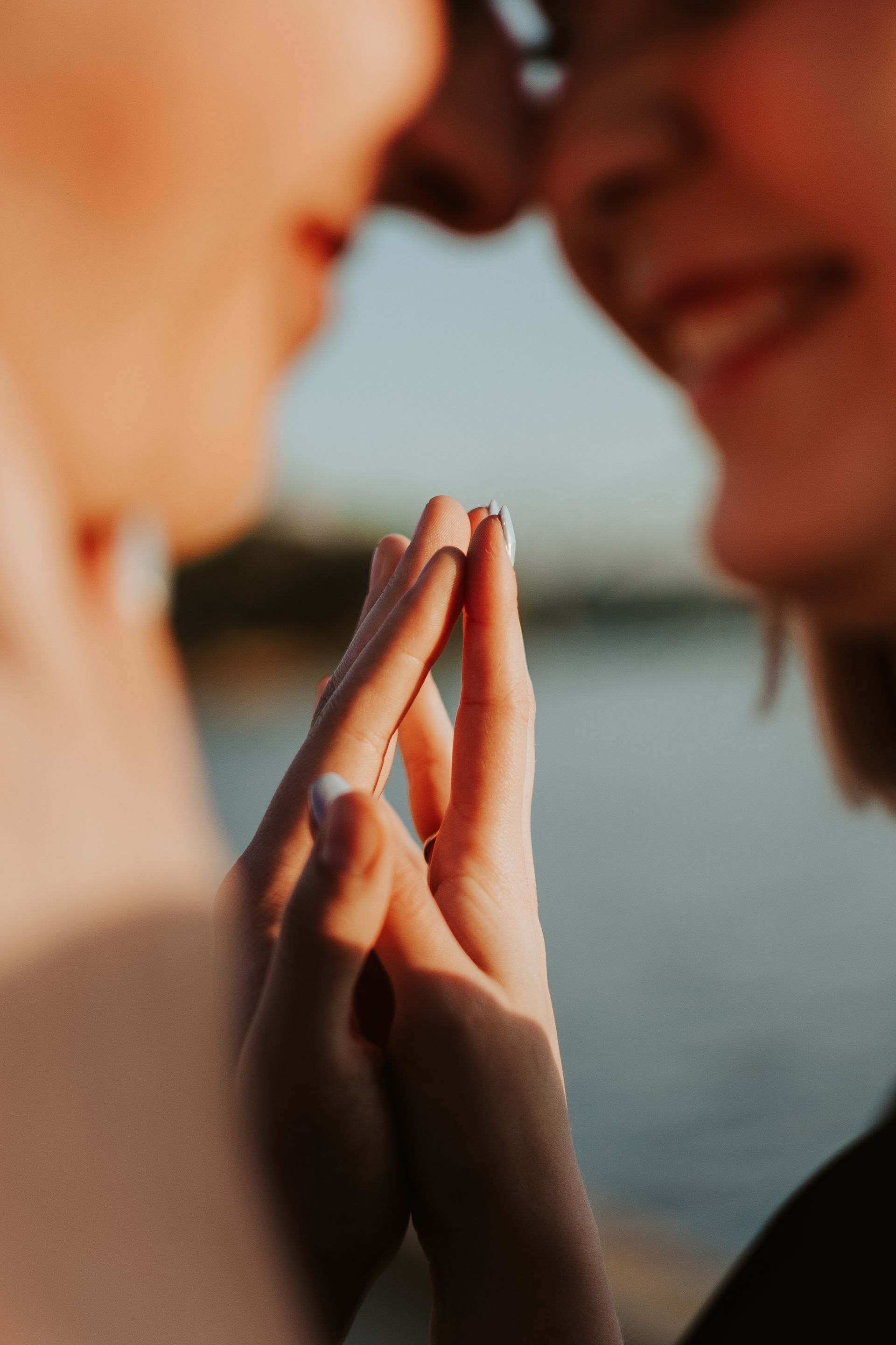 Two people touching fingertips in warm sunlight by the water