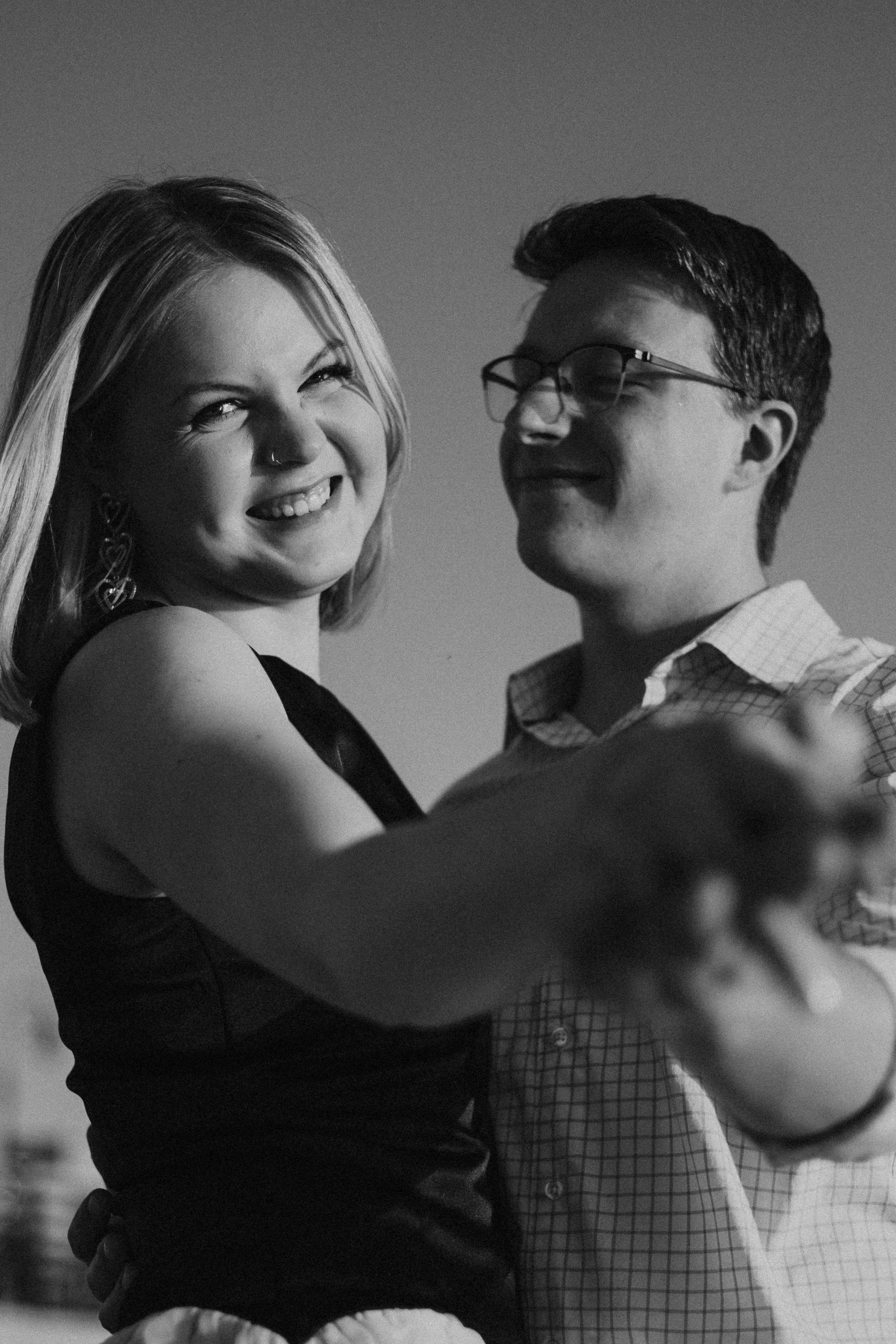 Smiling couple dancing closely, with the woman in front and the man holding her hand.
