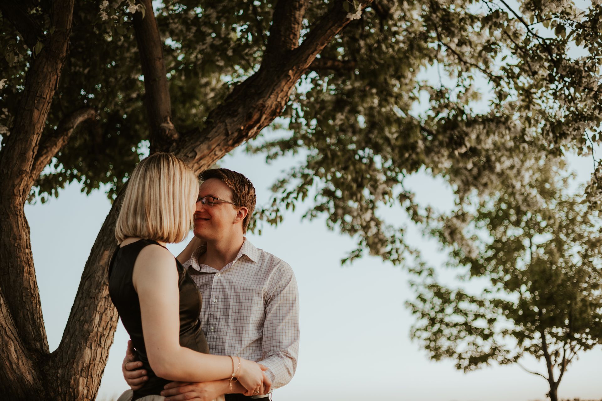 Couple embracing under a large tree, smiling in a sunlit outdoor setting