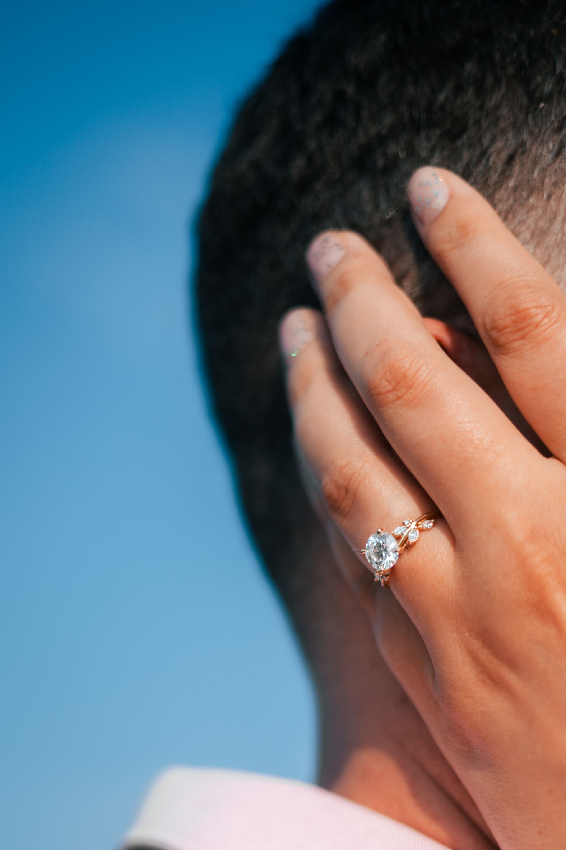 Close-up of a hand with a diamond ring touching the side of a person’s head against a blue background