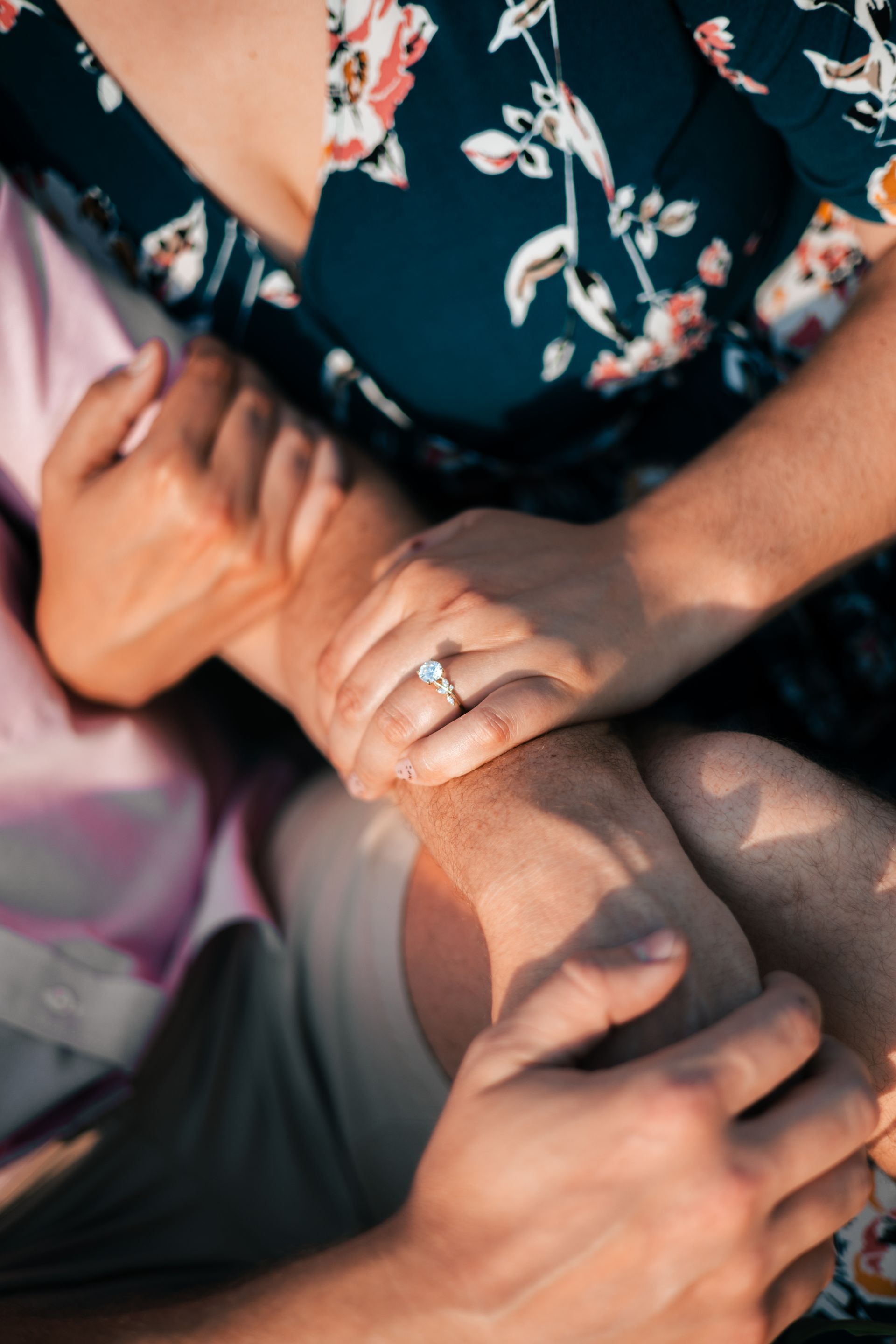 Hands with a ring resting on a floral dress in warm sunlight