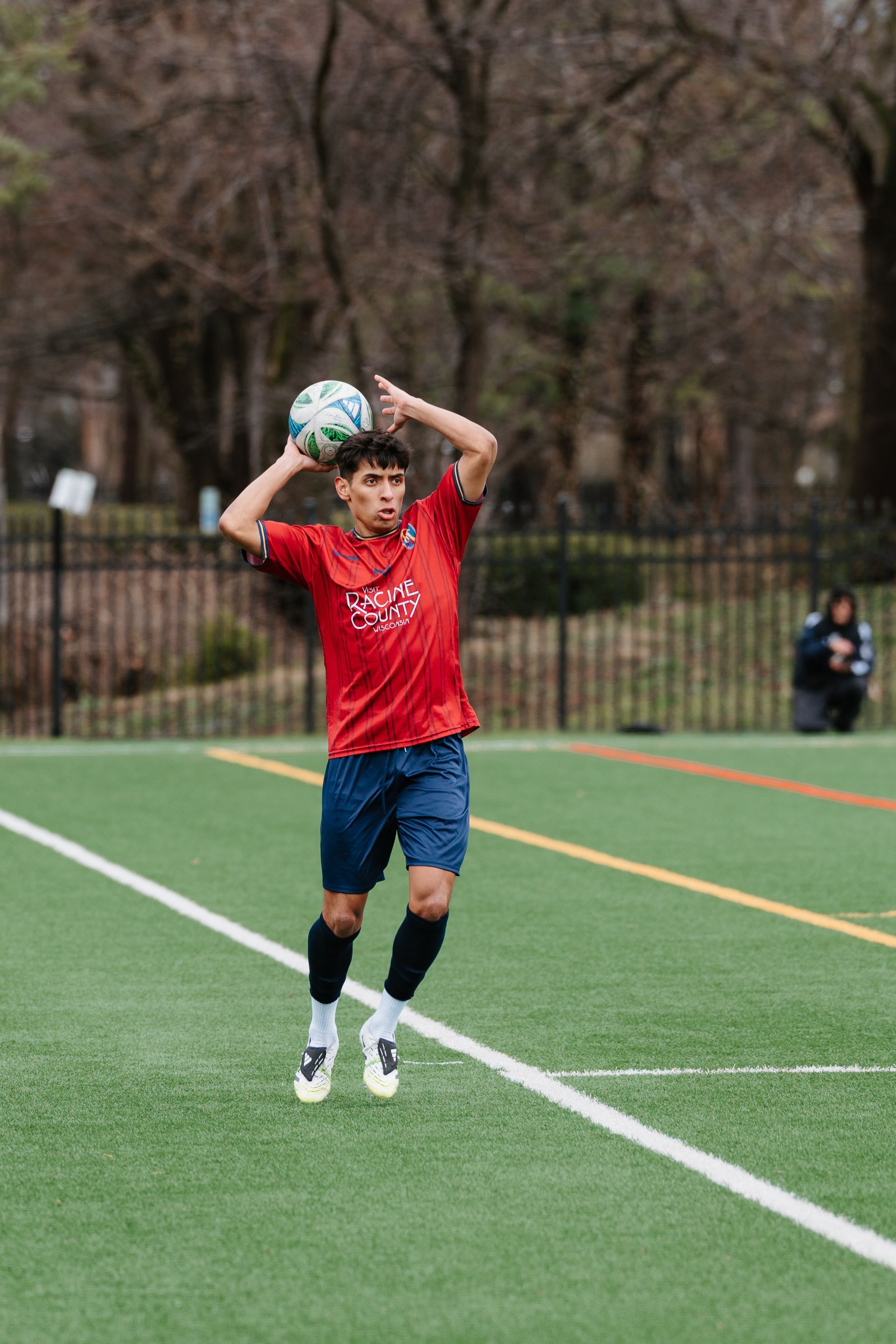 Soccer player in red jersey throwing the ball in on an outdoor field