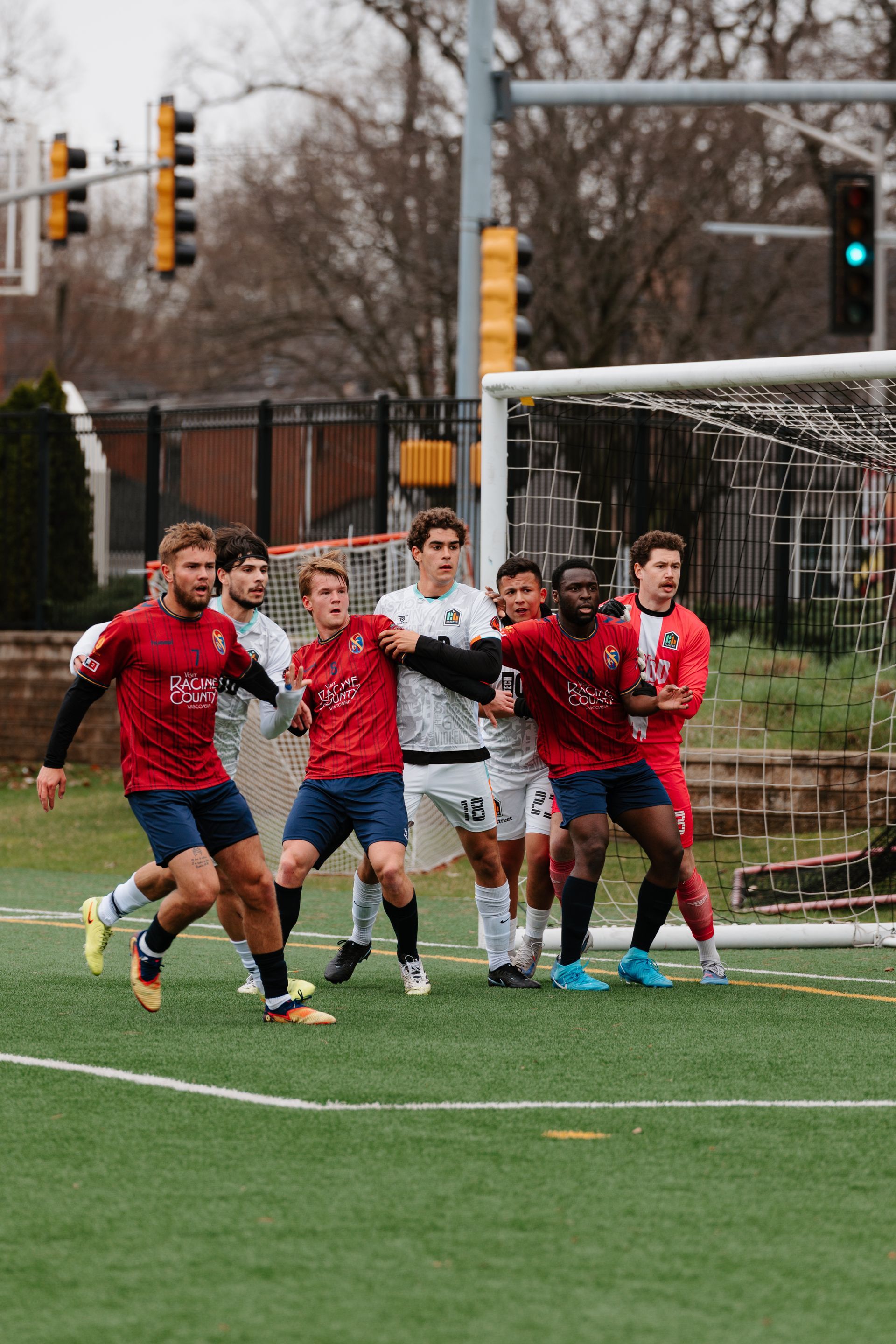 Soccer players in red jerseys sprint on a wet field during a match