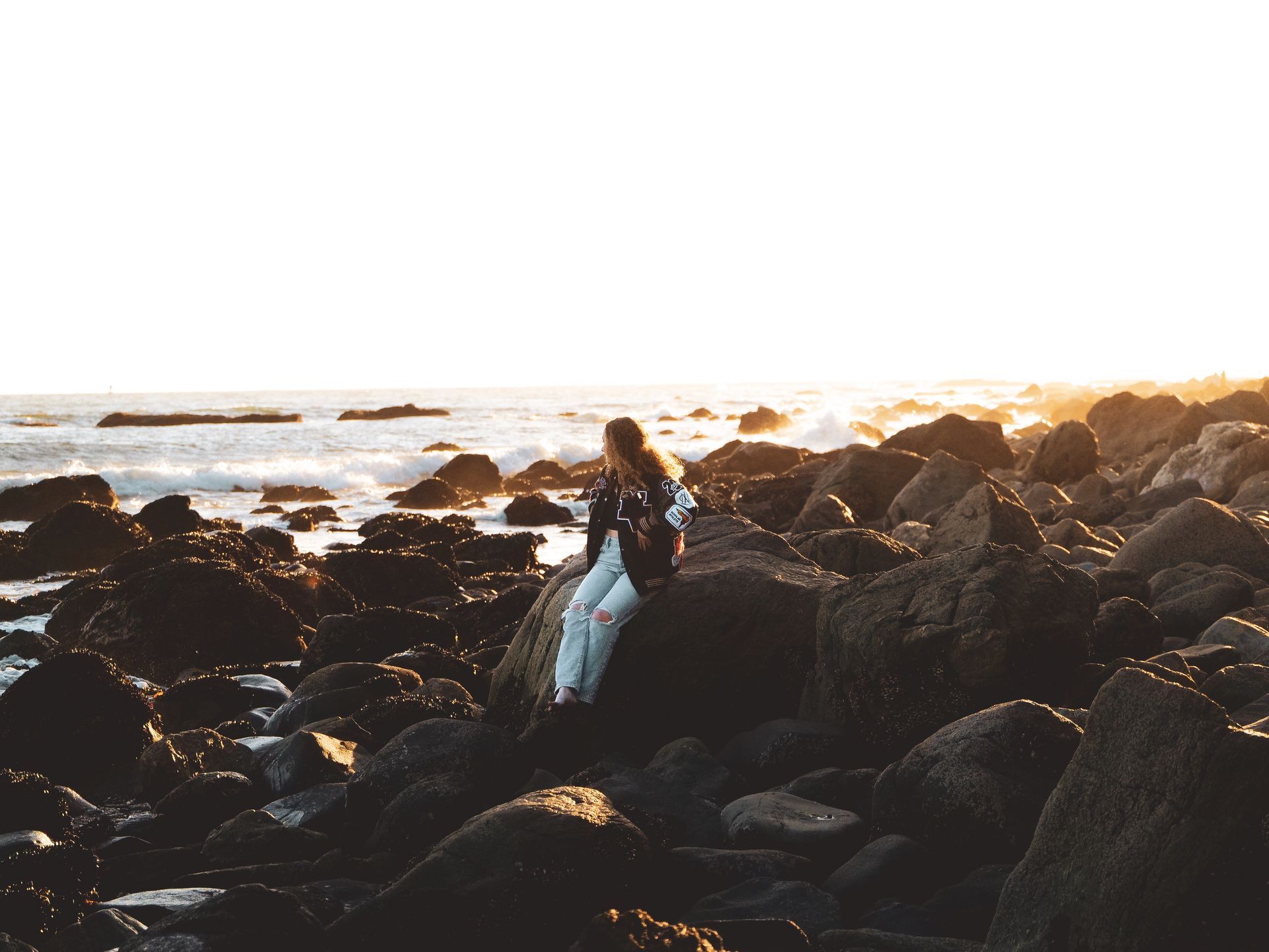 A woman is sitting on a rock near the ocean.