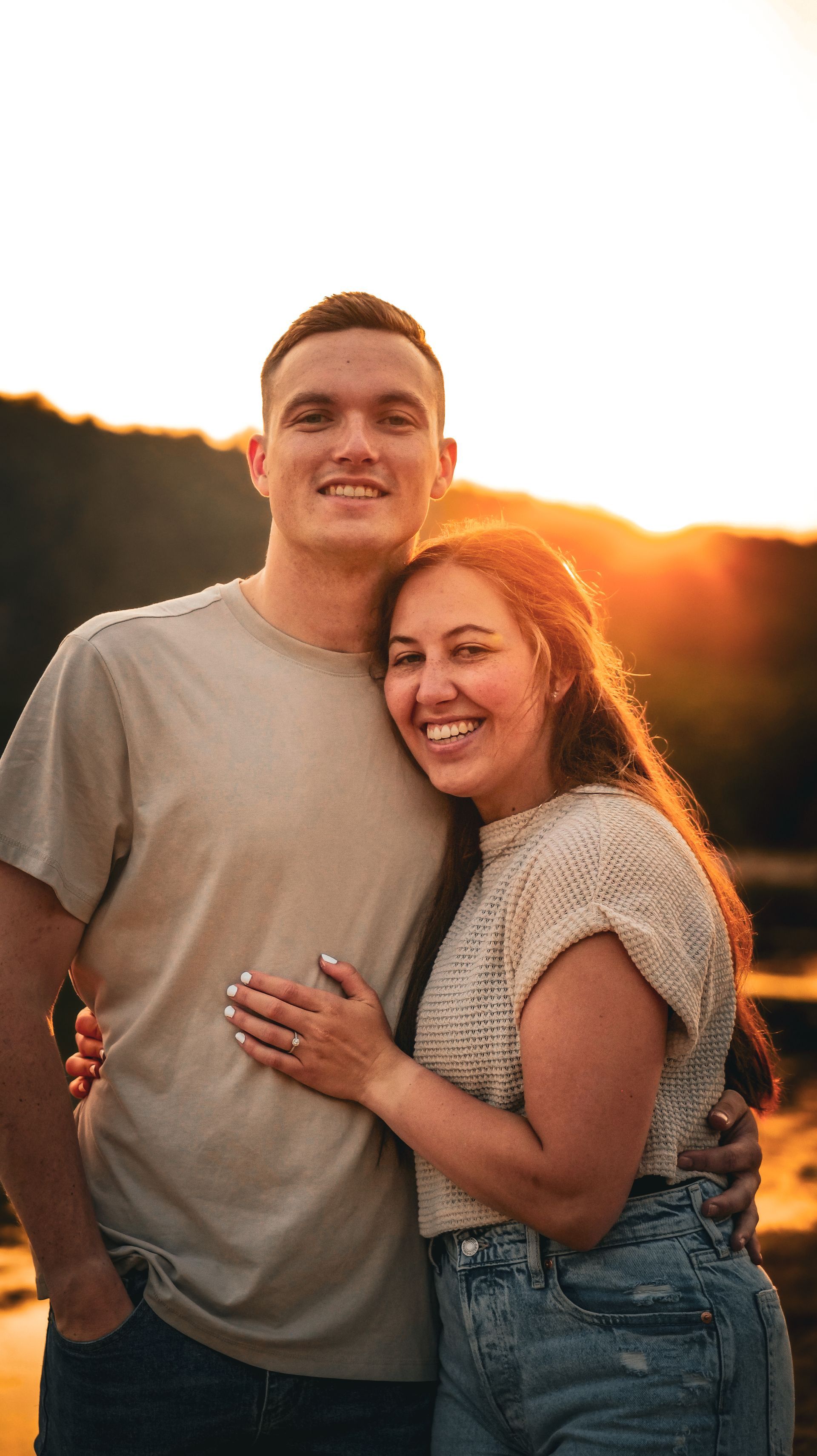 Smiling couple embracing outdoors at sunset, with warm golden light behind them