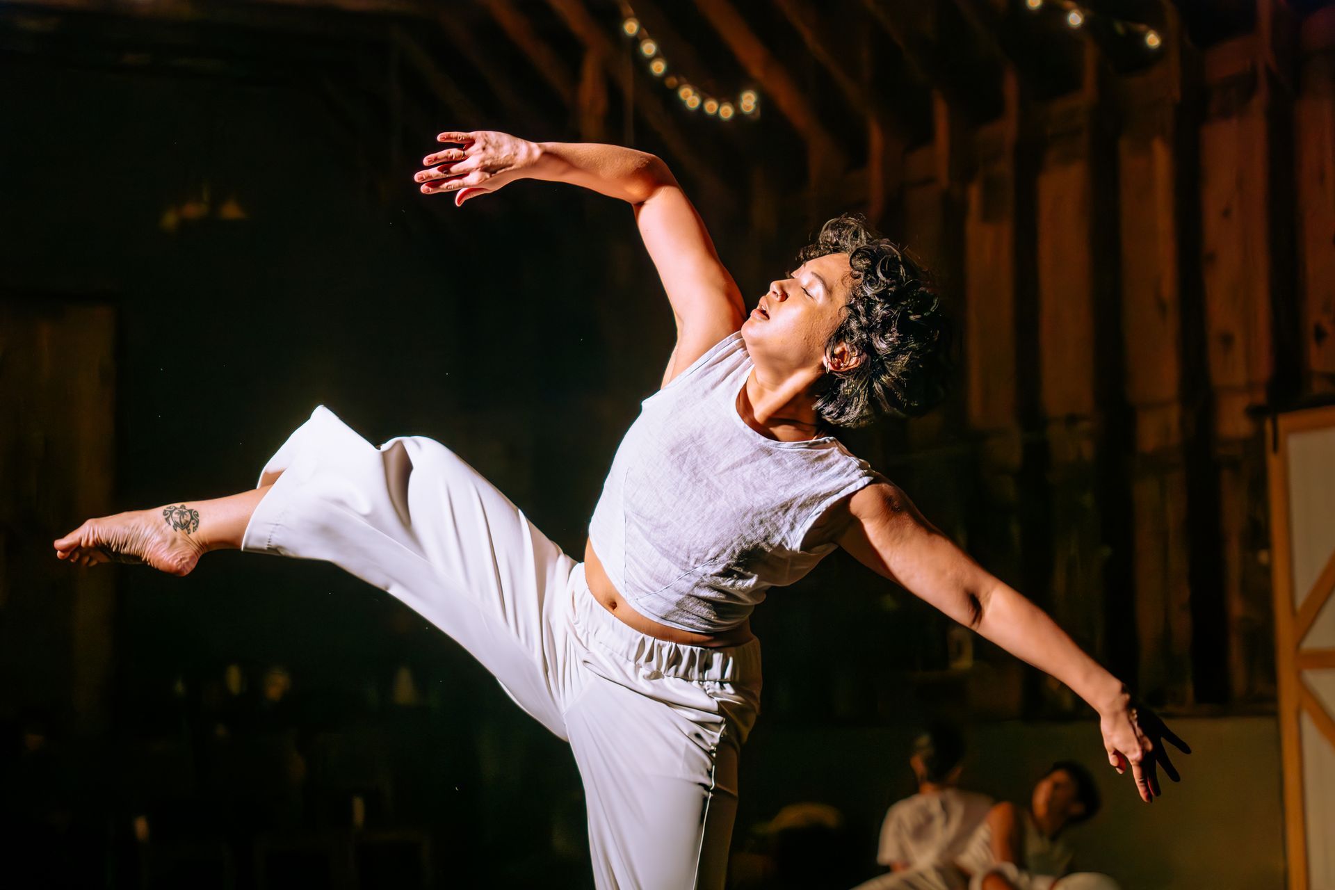 Dancer in white raises one leg and arm on a dim stage with warm lights