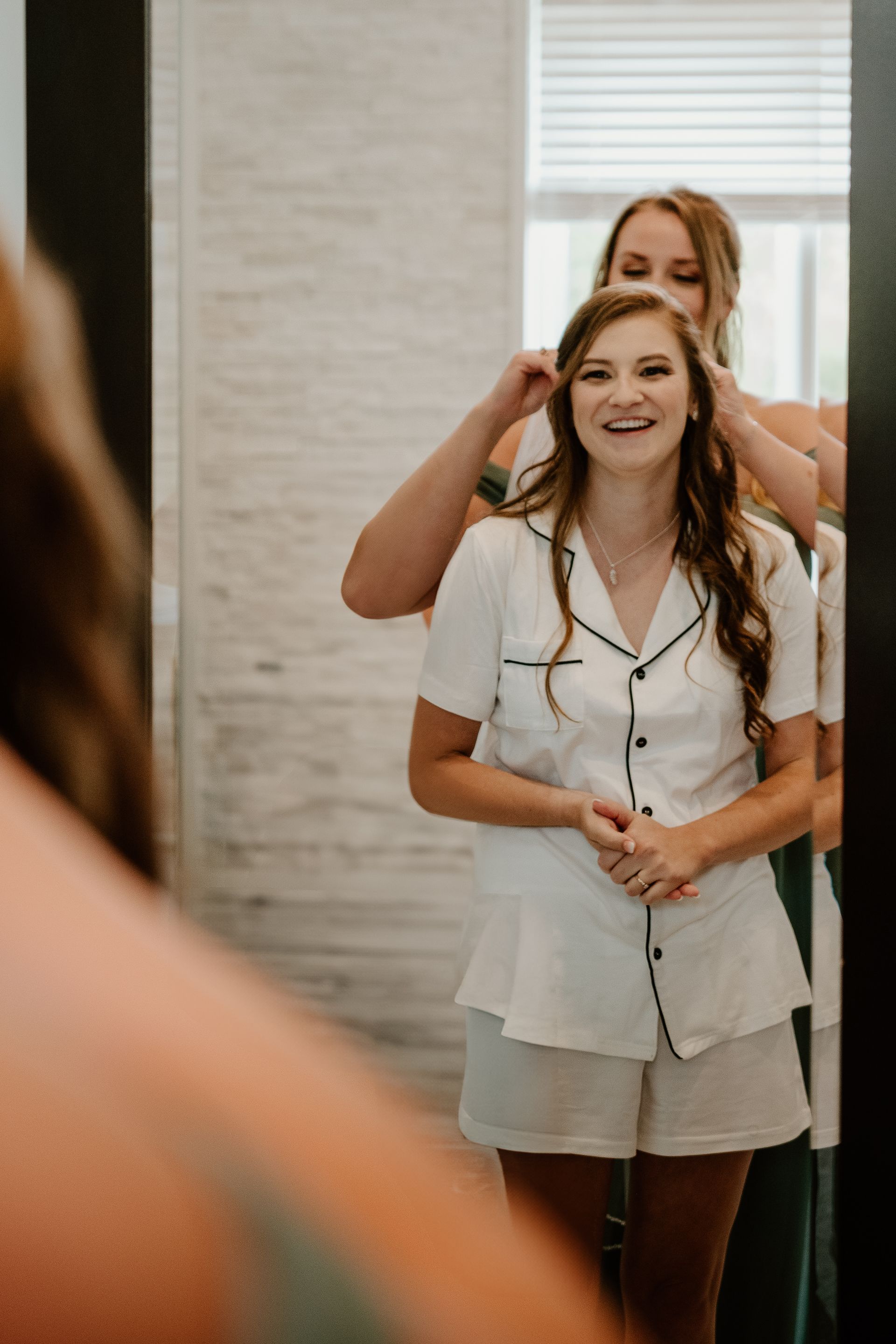 Woman smiling while another person styles her hair in a bright room with a window.