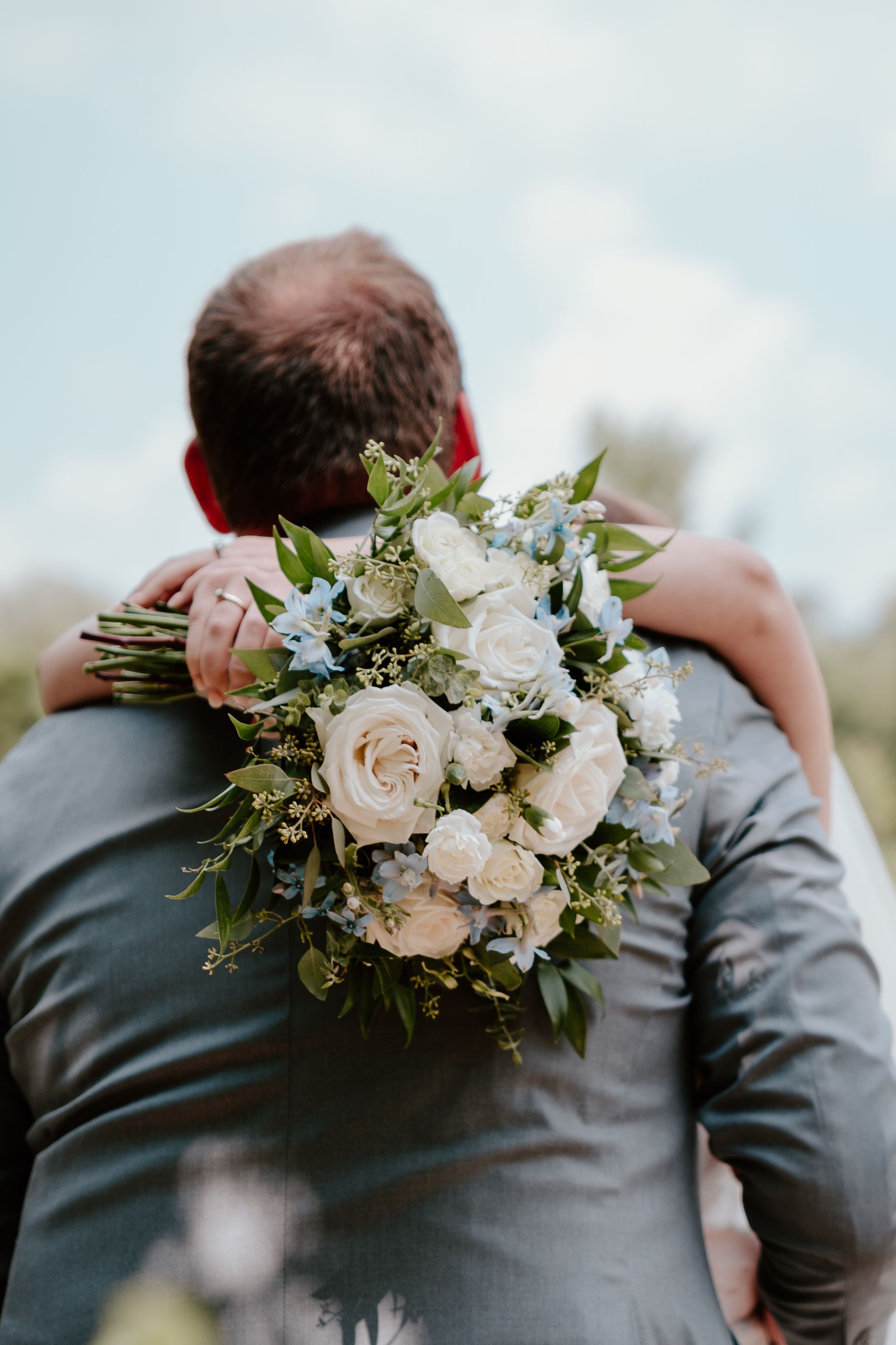 Person carrying a large white flower bouquet on their back outdoors against a cloudy sky