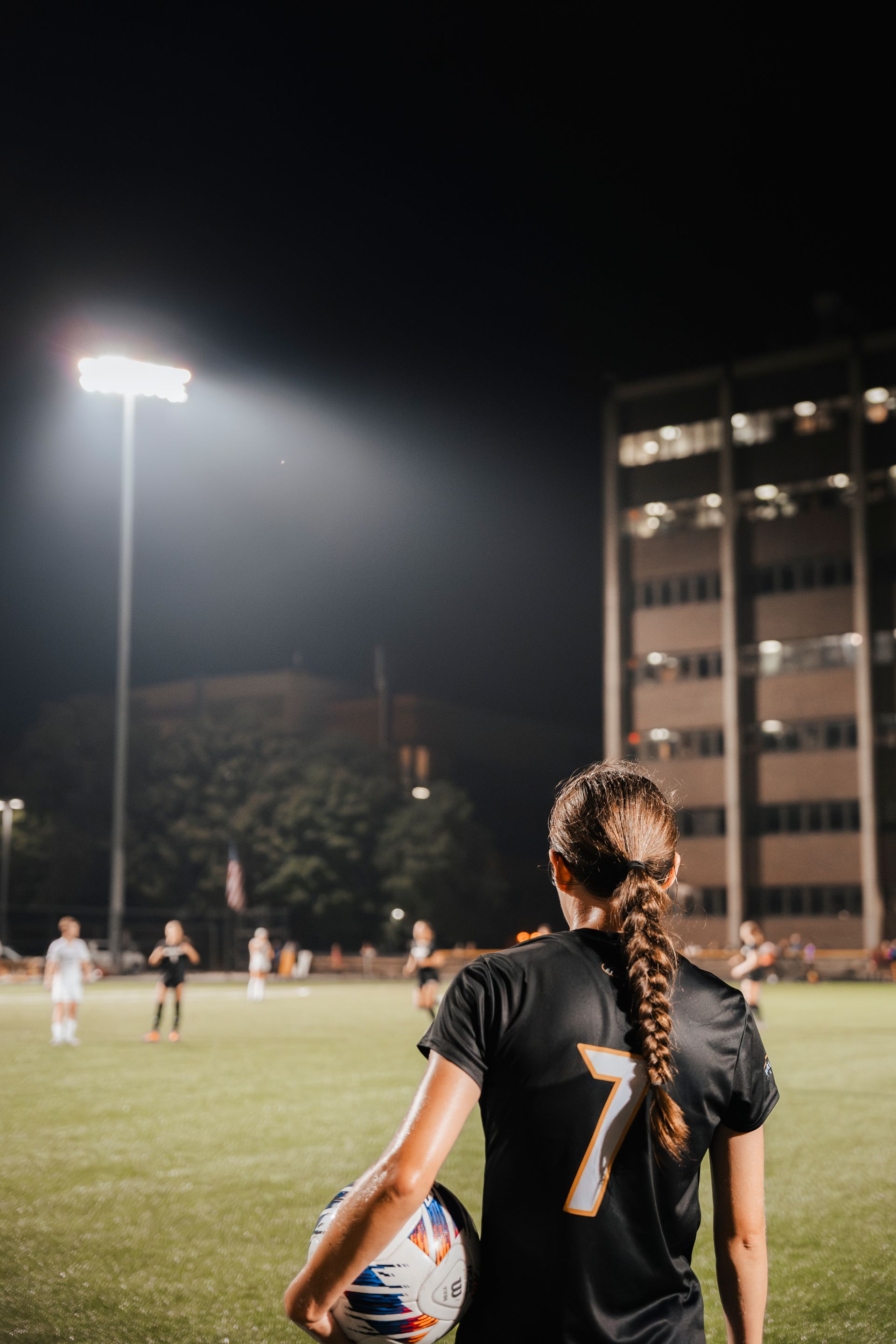 Soccer player in black jersey with number 7 watches a night game under bright stadium lights