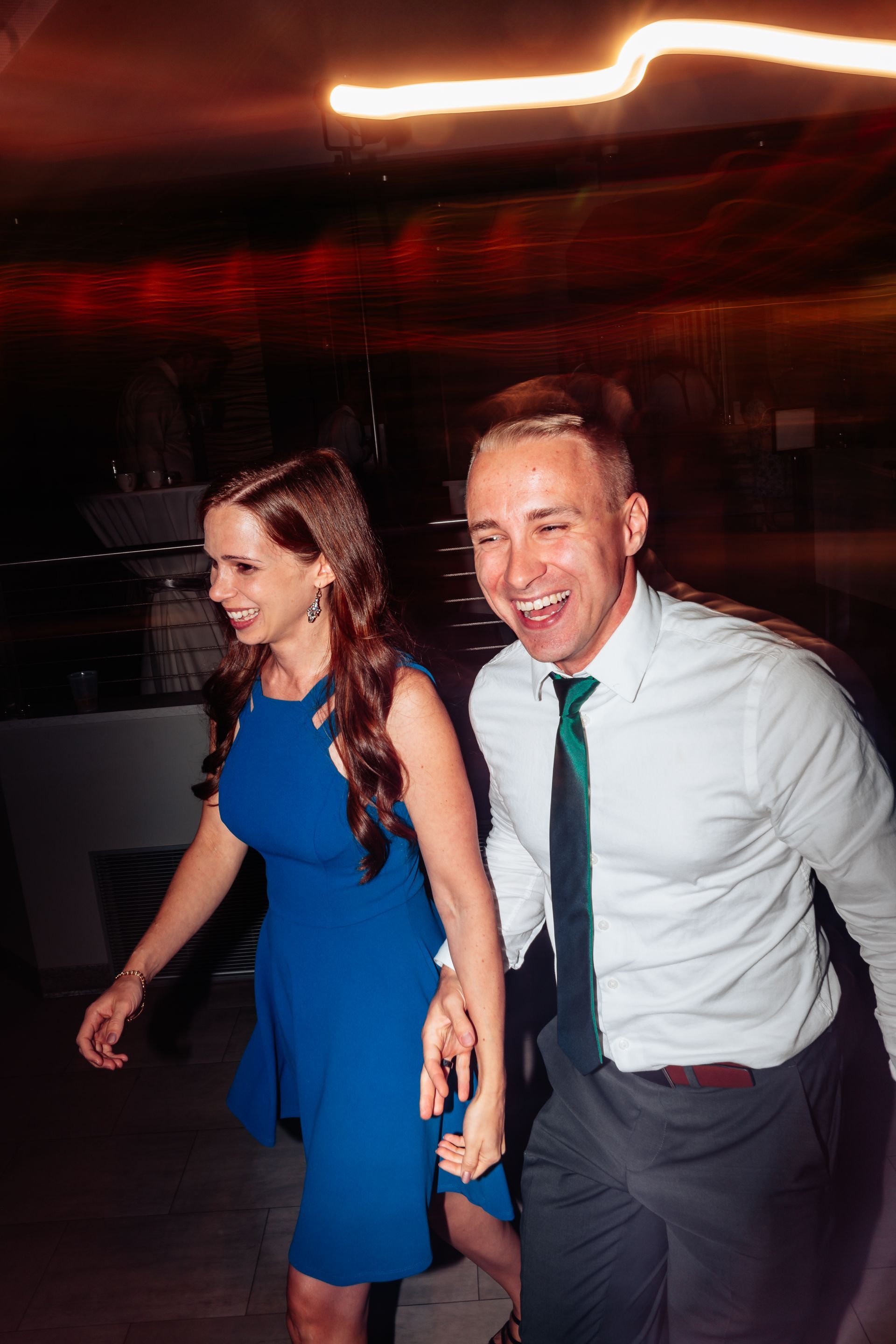 Two people dancing at a dimly lit party, smiling and holding hands, with motion blur in the background.