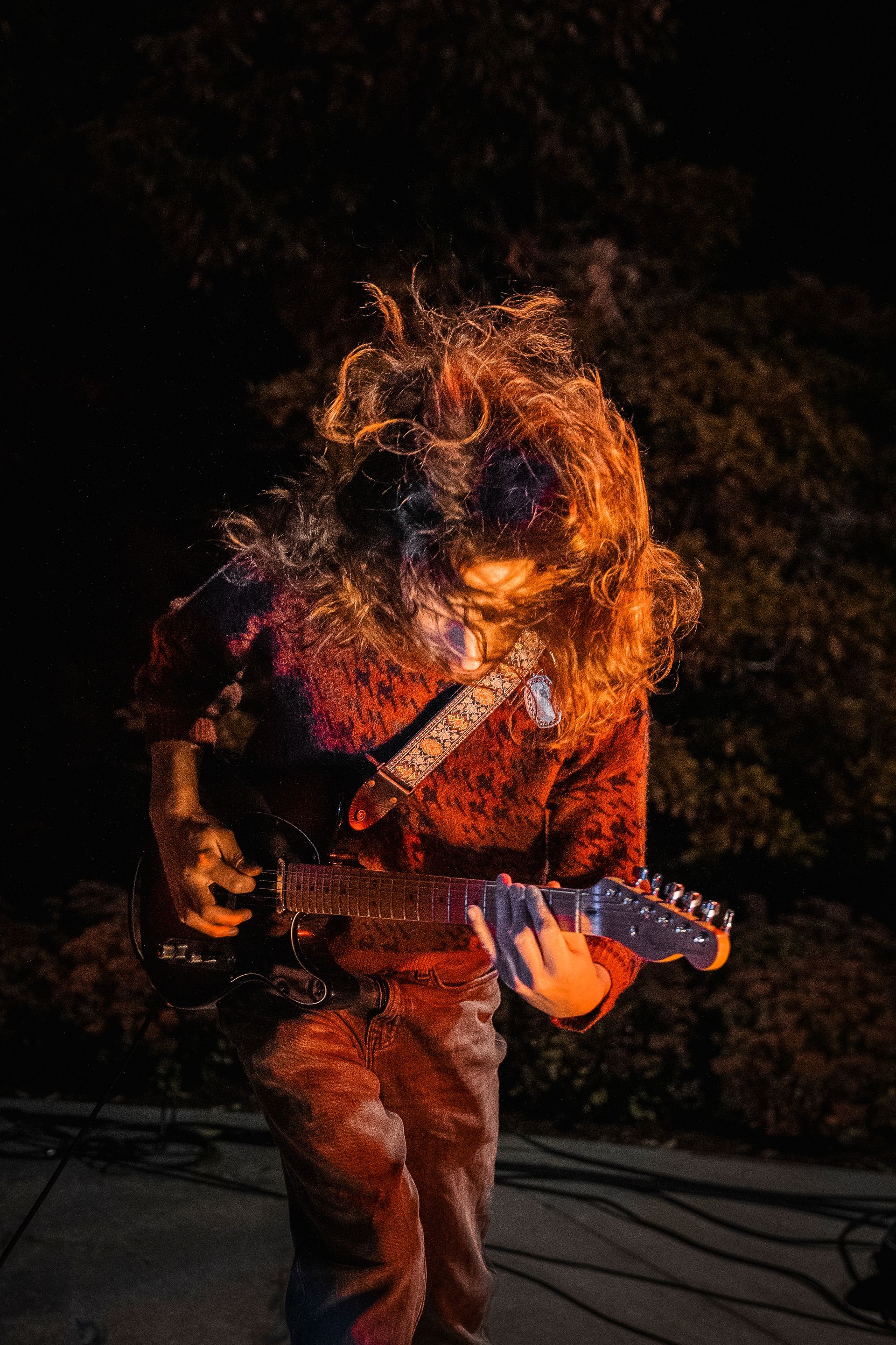 A man with long hair is playing a guitar in the dark.