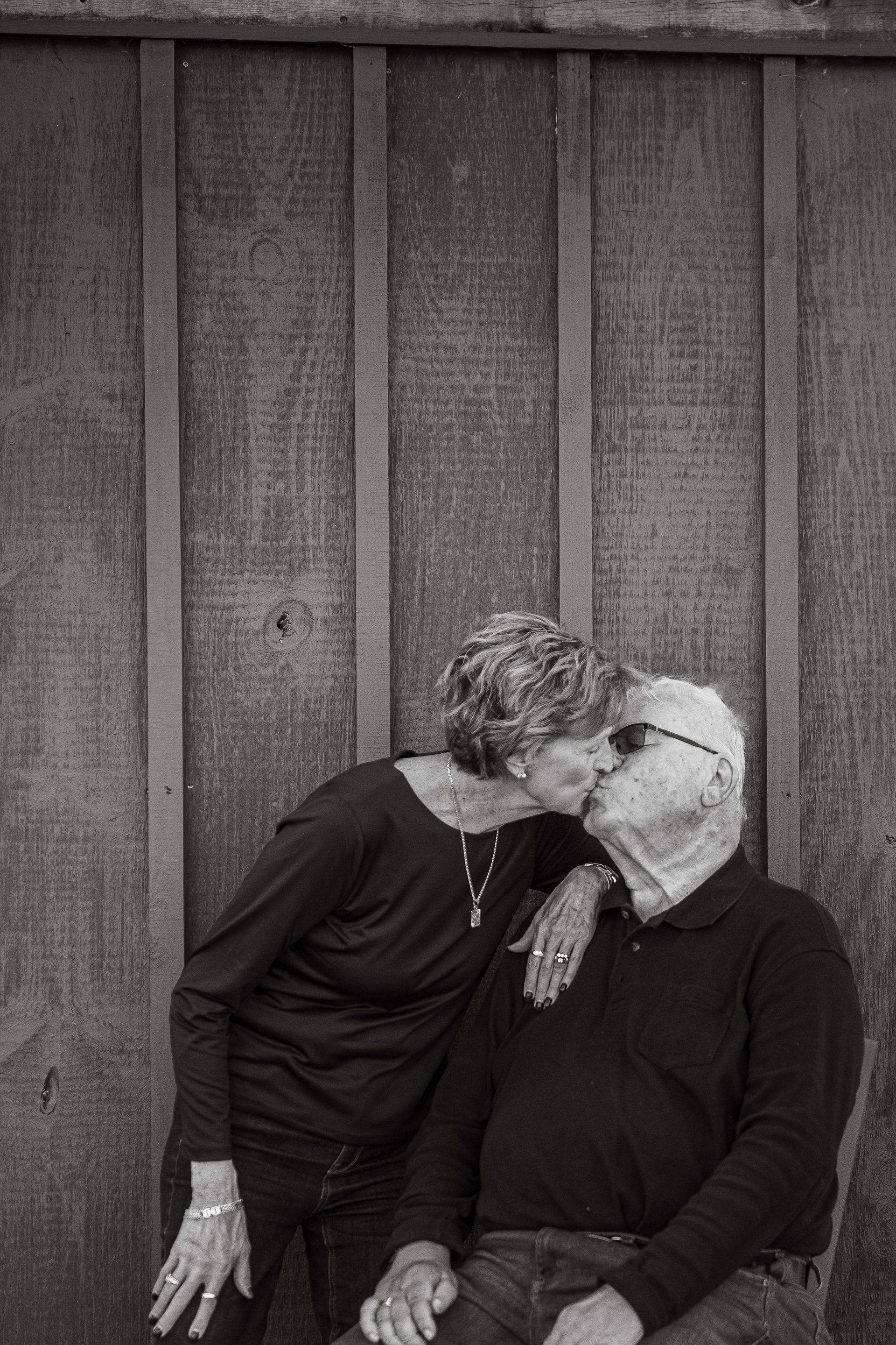 A man and a woman are kissing in front of a wooden wall.