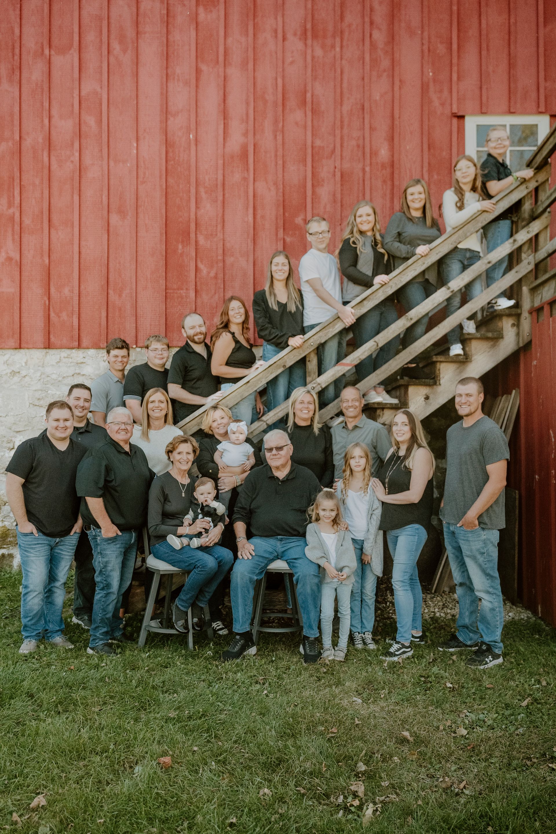 A large family is posing for a picture in front of a red barn.