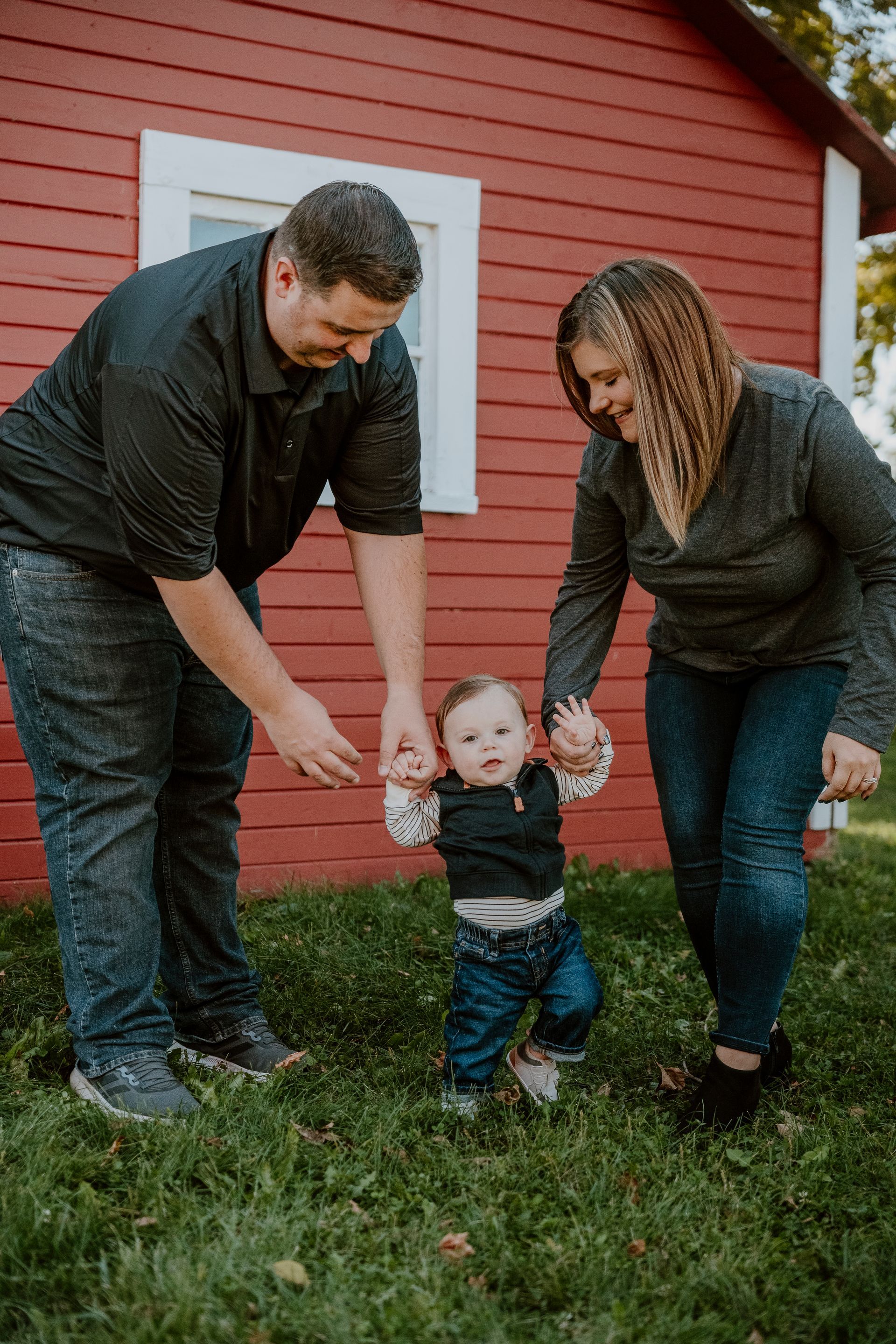 A family is standing in front of a red barn holding hands.