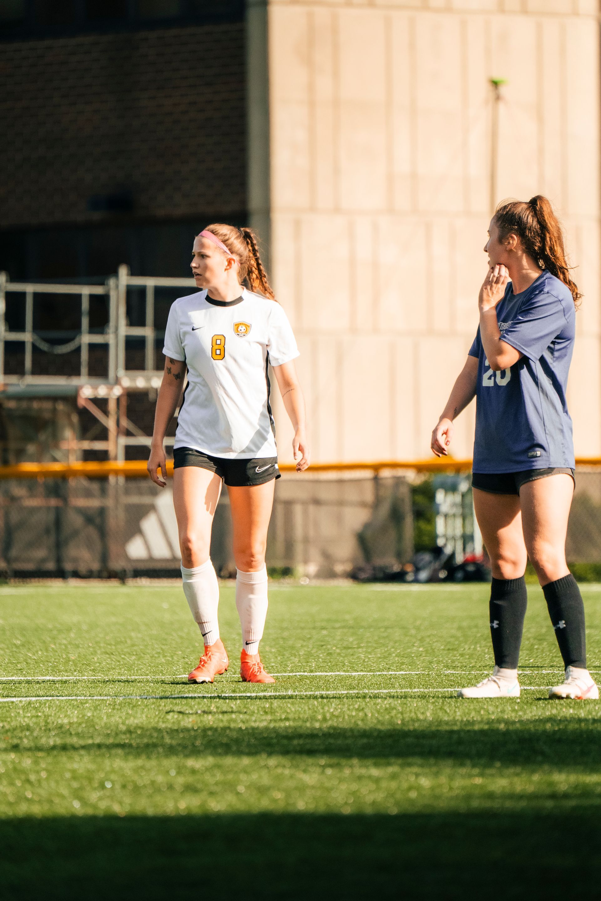 Two soccer players standing on a lit field, one in white and one in blue, during practice.