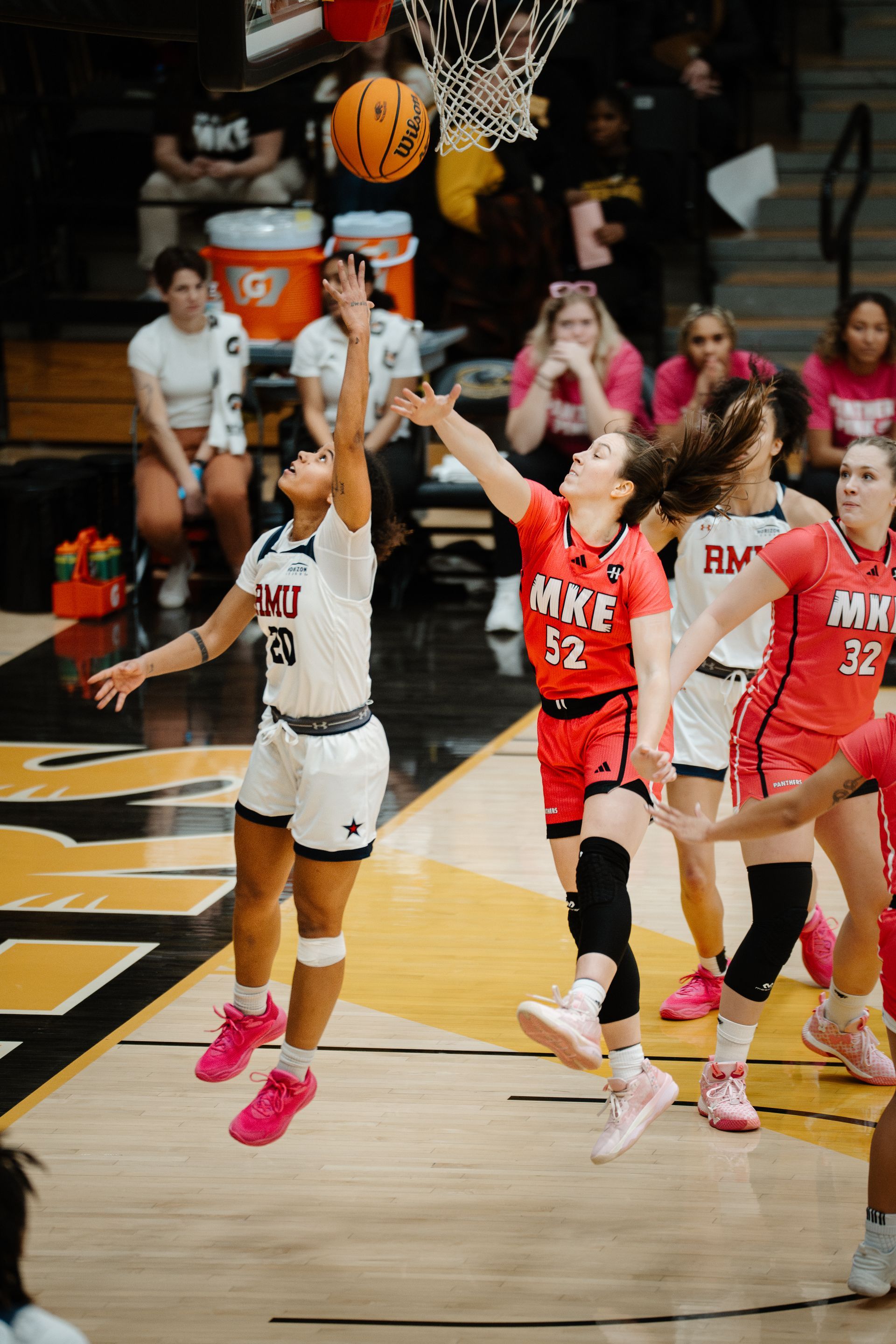 Basketball player in white shoots near the hoop as defenders in red contest the play