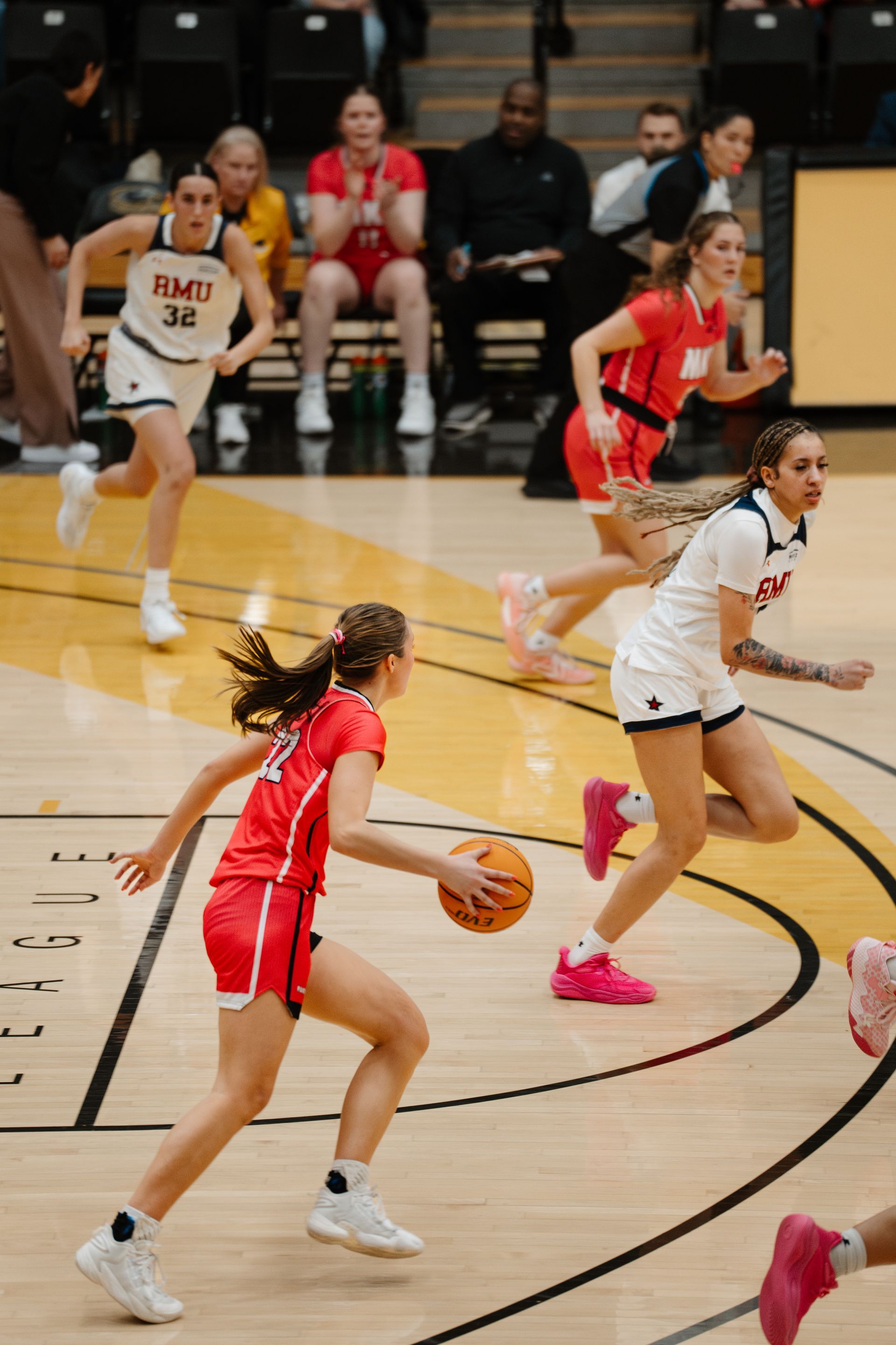 Women’s basketball game with a player dribbling past defenders on an indoor court