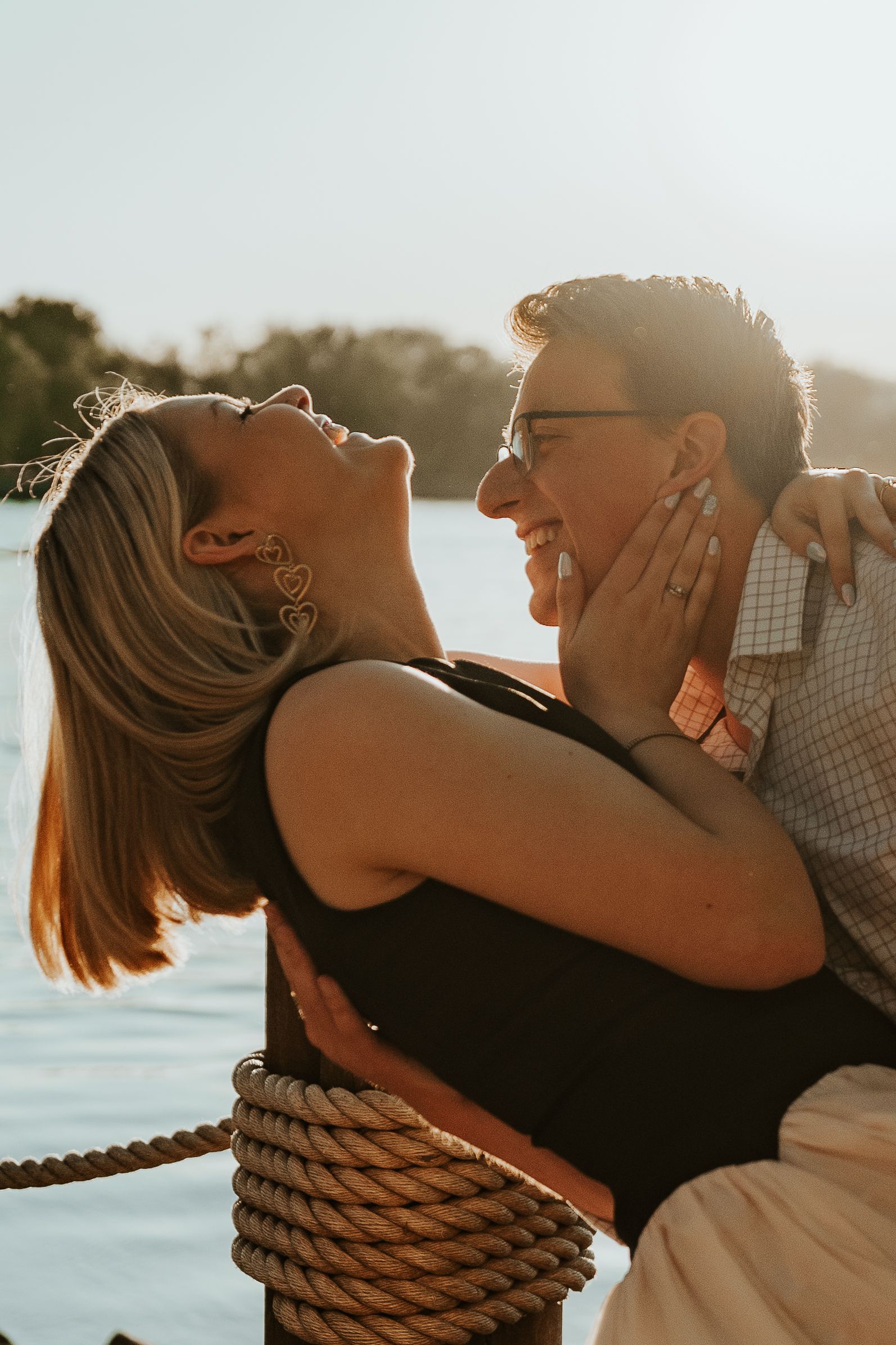 Couple laughing and embracing on a boat at sunset, with warm backlighting and water in the background