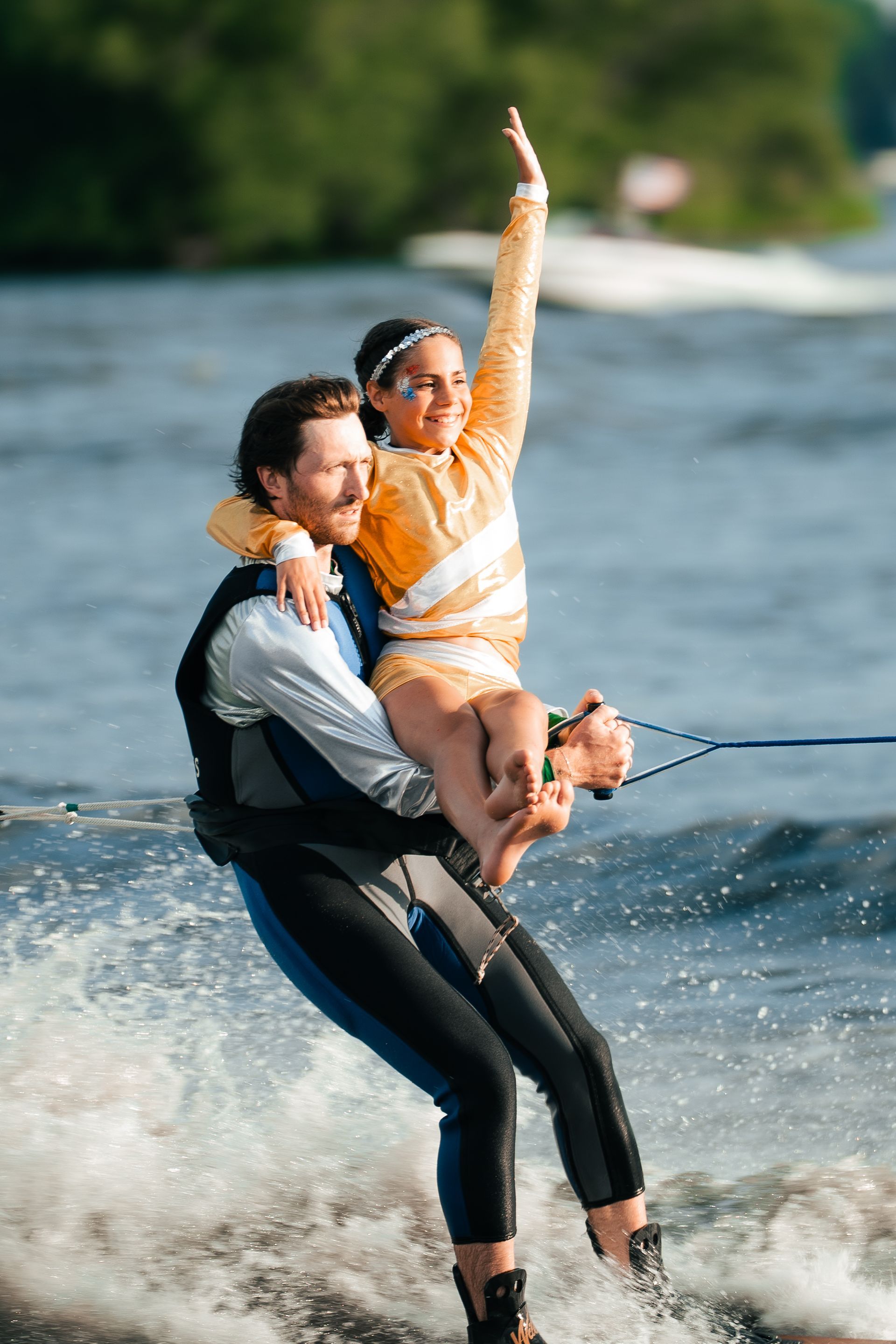 Two people waterskiing, one raising an arm on a lake with a spray of water