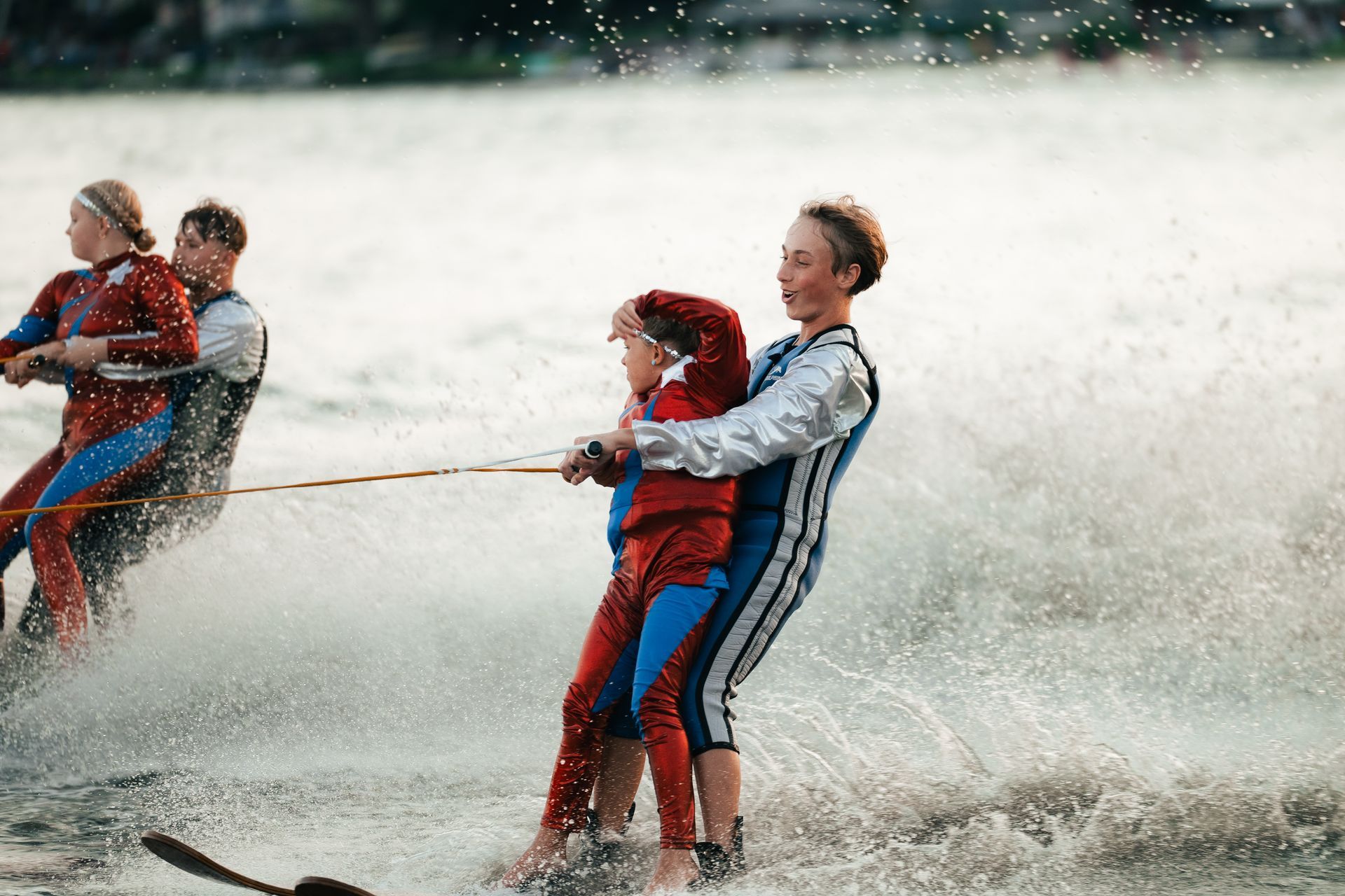 People water skiing in a spray of water, holding onto a tow rope in a lake.