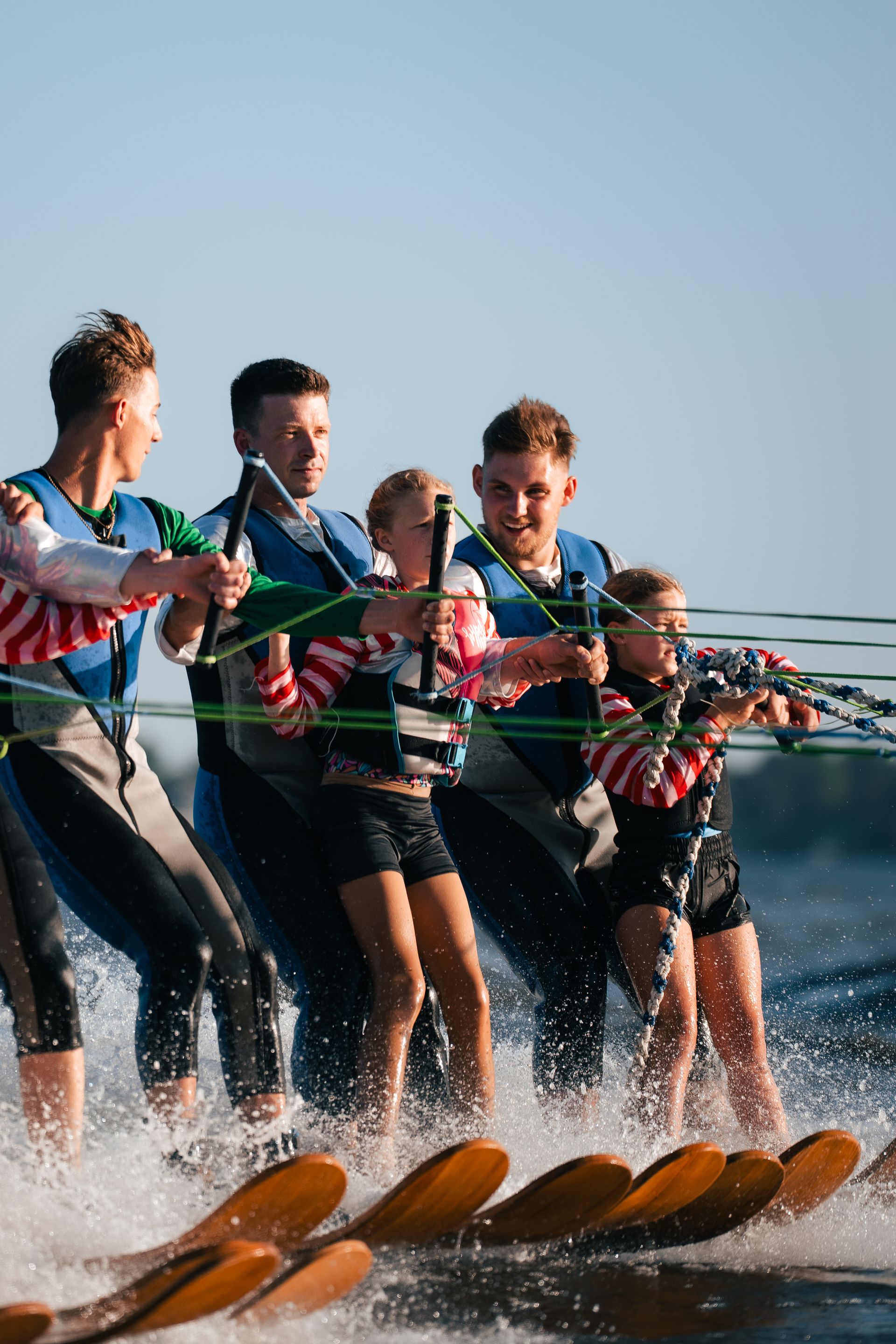 People water skiing in a line, spraying water, with one skier leading at the front.