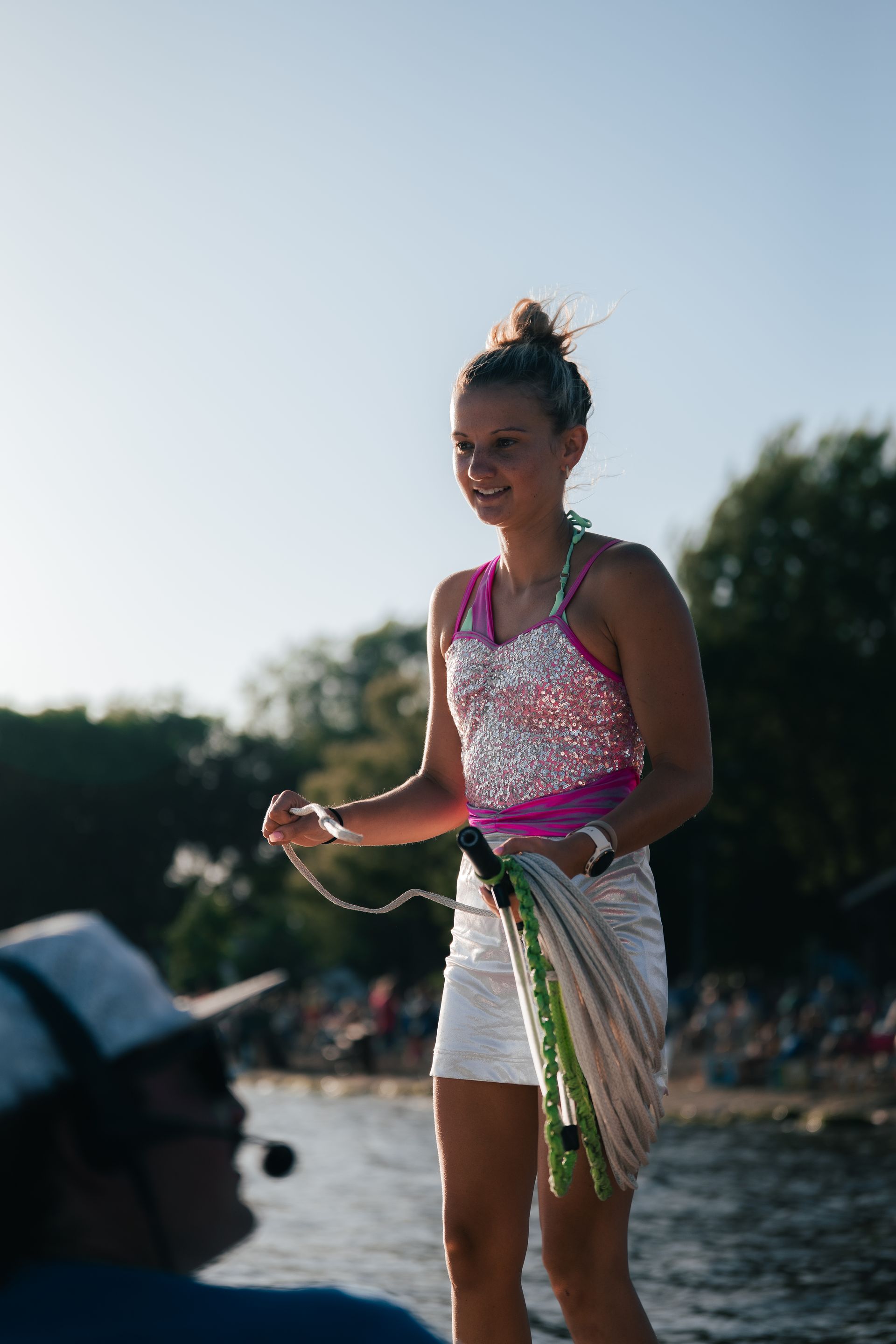 Woman in a pink top and white shorts holding a rope on a beach at sunset
