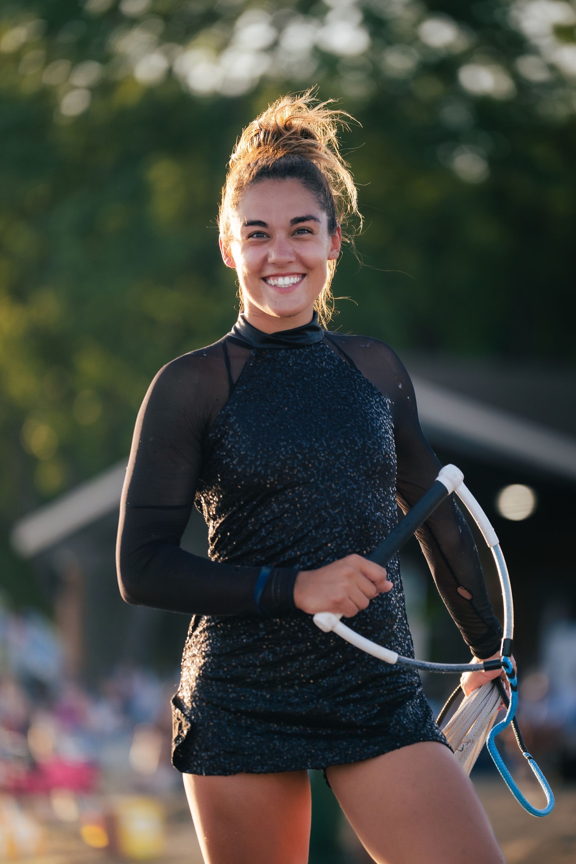 Tennis player in a black outfit holding a racket, smiling on an outdoor court at sunset