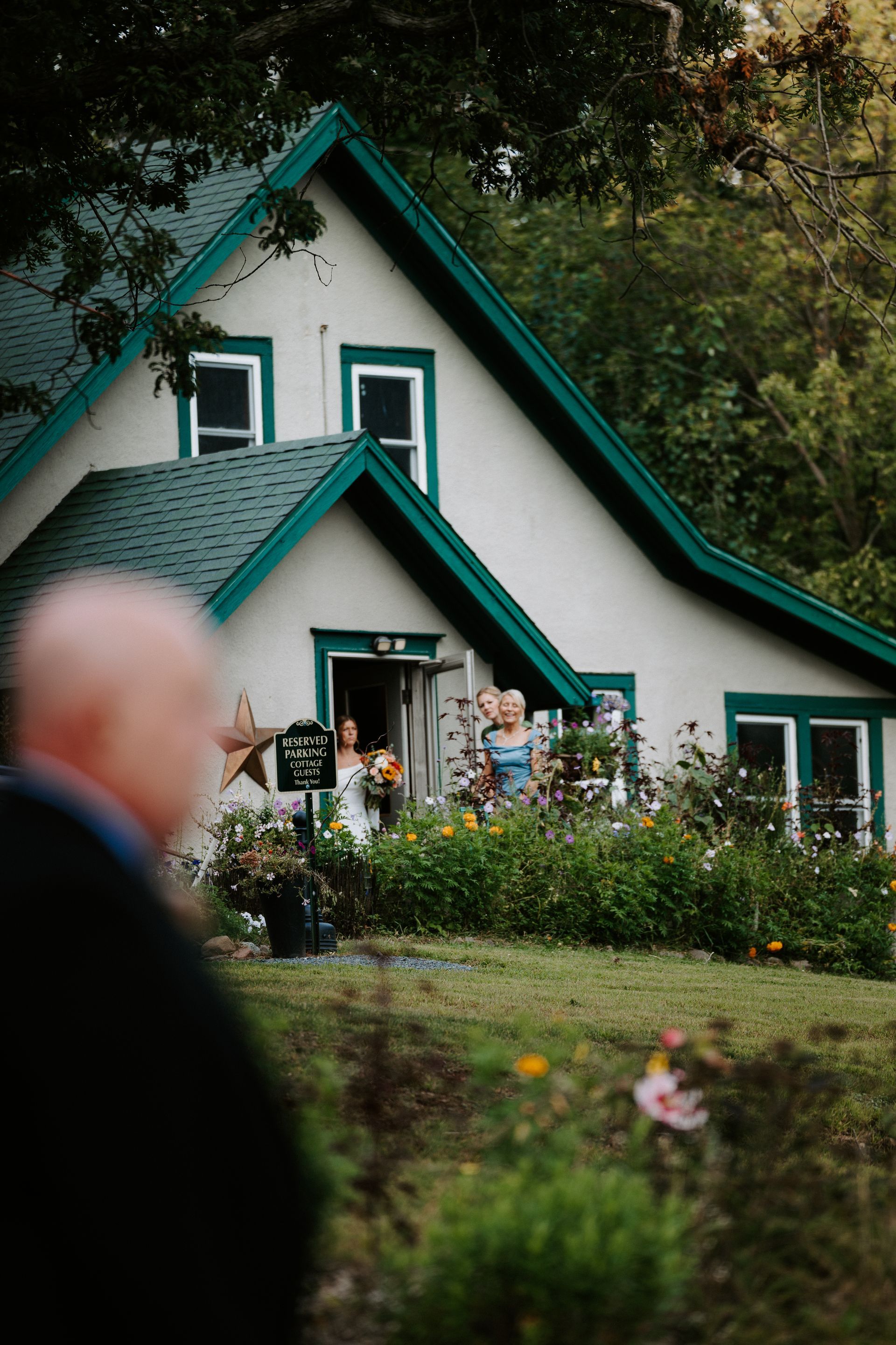 People gathered outside a white house with teal trim in a green garden.