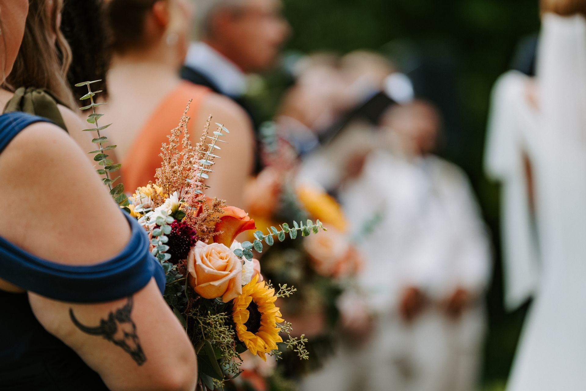 Bride holding colorful bouquet at an outdoor wedding, with blurred guests in the background