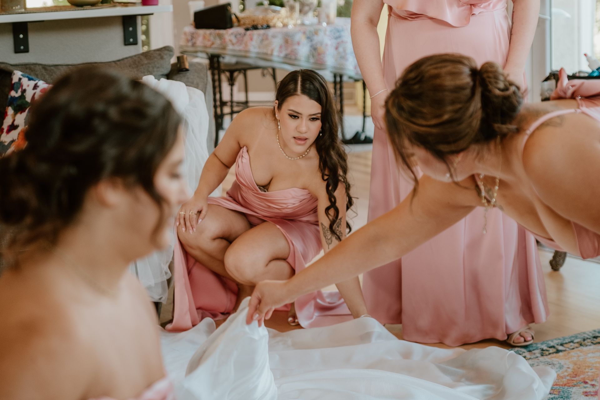 Bridesmaids in pink dresses gather around a gift table, reaching for a present at a bridal shower.