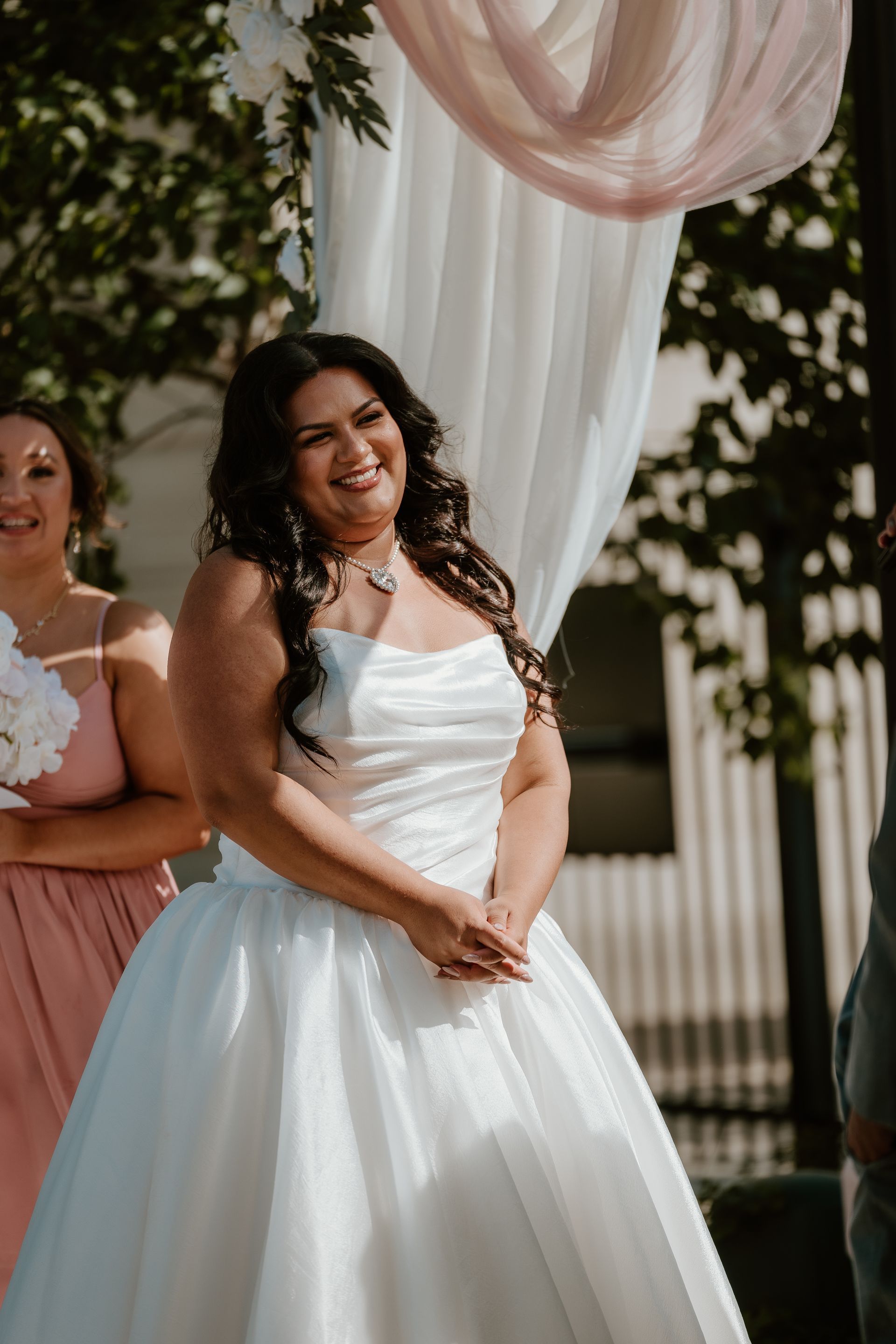Woman in a white wedding dress smiling under a draped canopy outdoors
