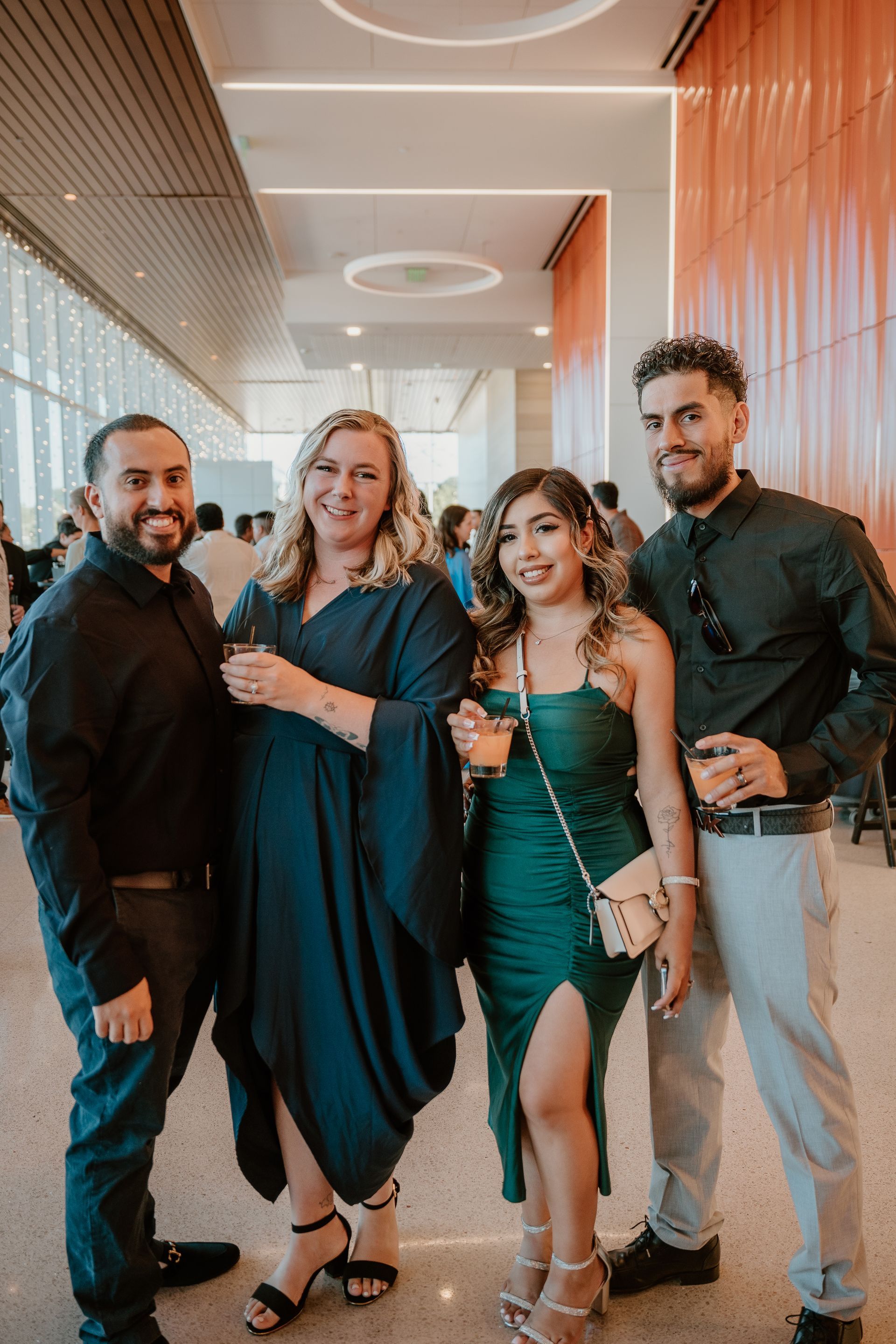 Four people pose together in a modern hallway, dressed in formal dark and teal outfits.