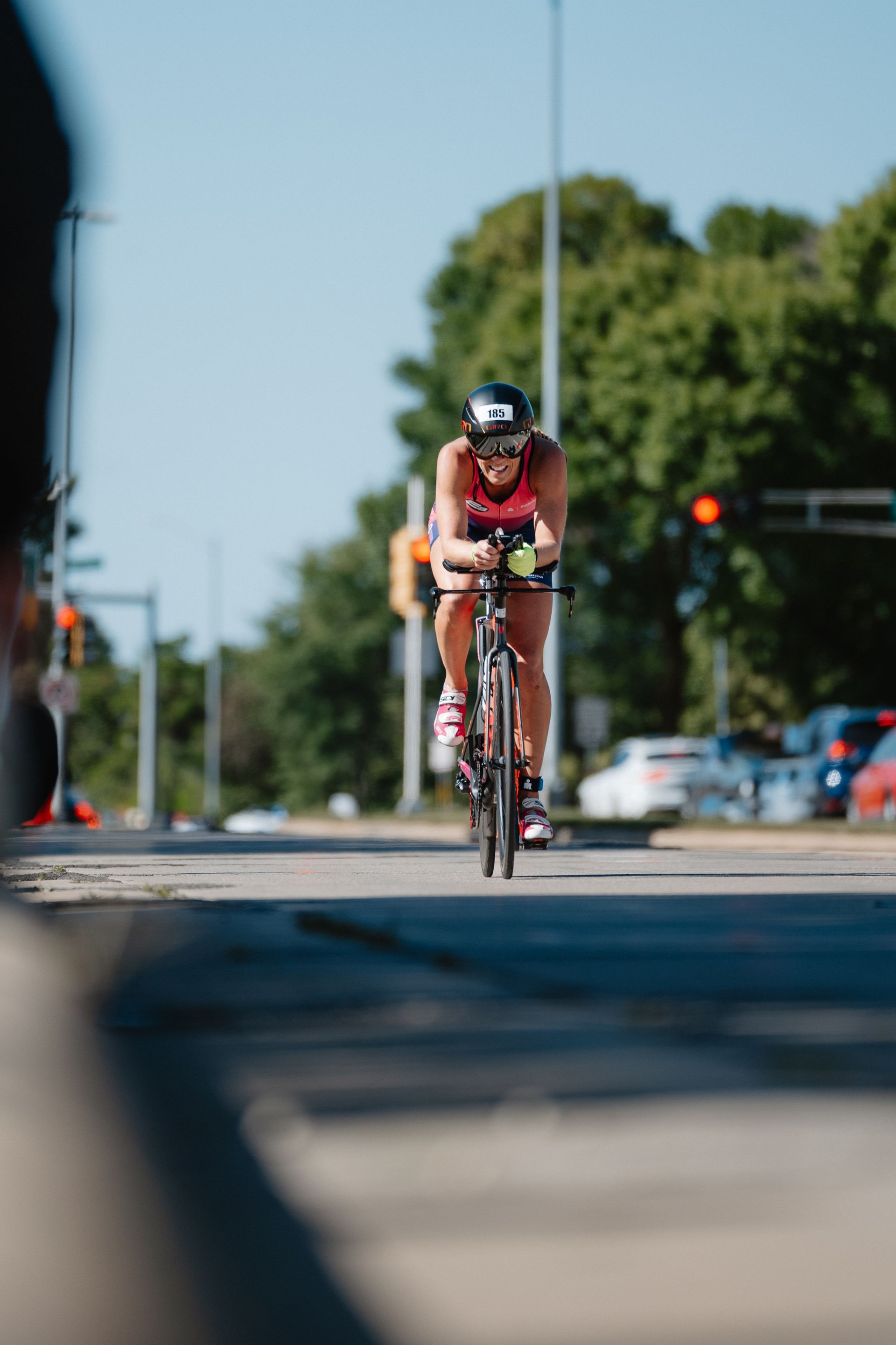 Cyclist in red racing down a sunlit city street with trees and traffic lights in the background