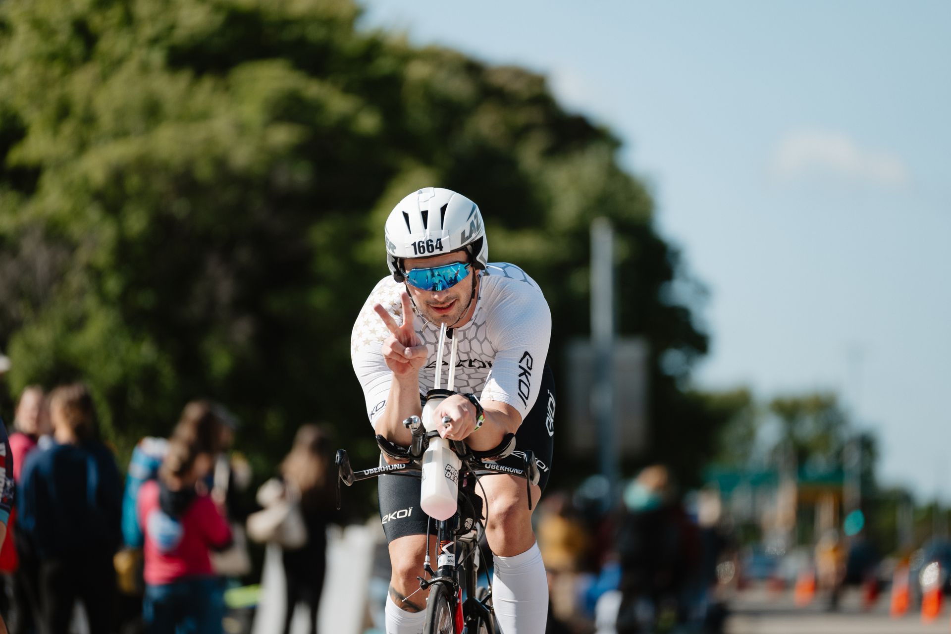 Cyclist in white racing through a road race, leaning forward with focused effort, spectators blurred in background
