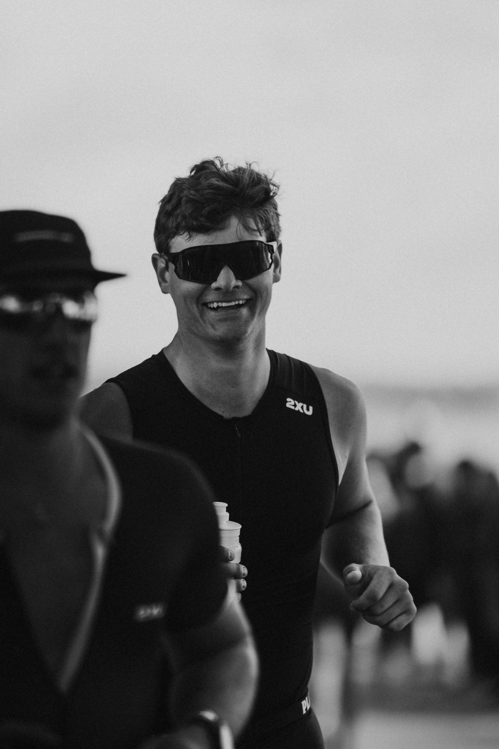 Smiling runner wearing sunglasses and a black shirt, running outdoors in a crowd