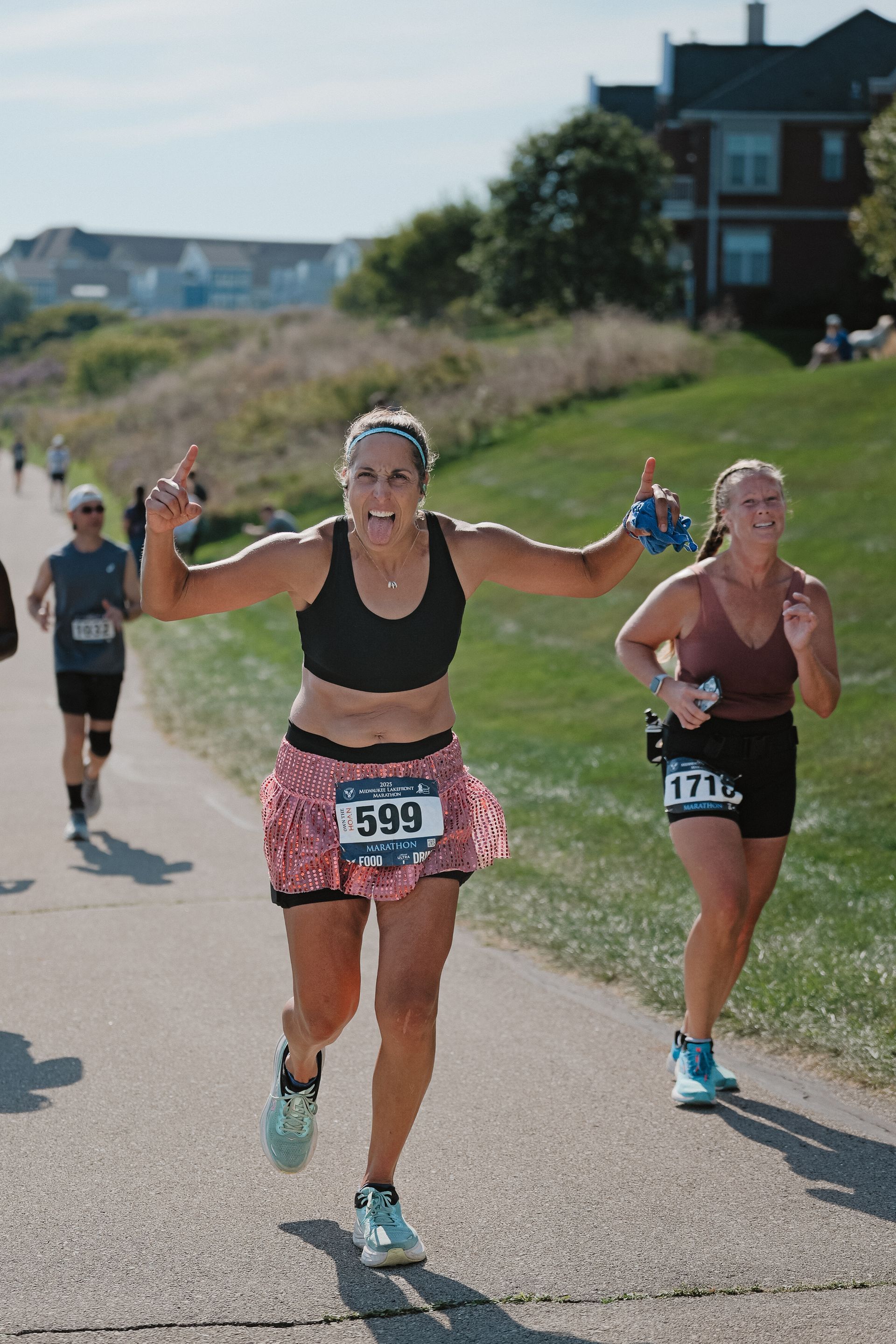 Runners on a coastal path, with one smiling and raising both arms near the finish.