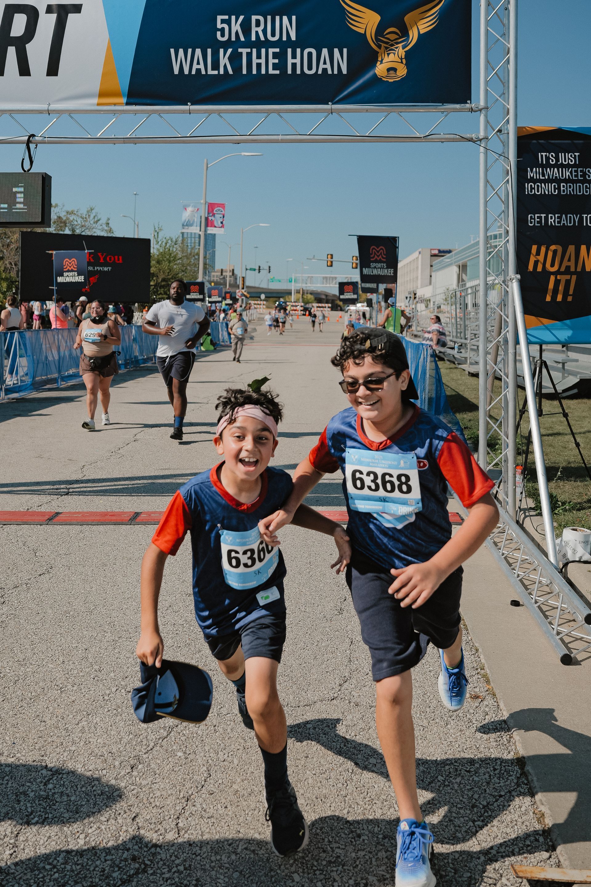 Two runners in bibs sprint through a race finish area under a “5K Run / Walk” banner.