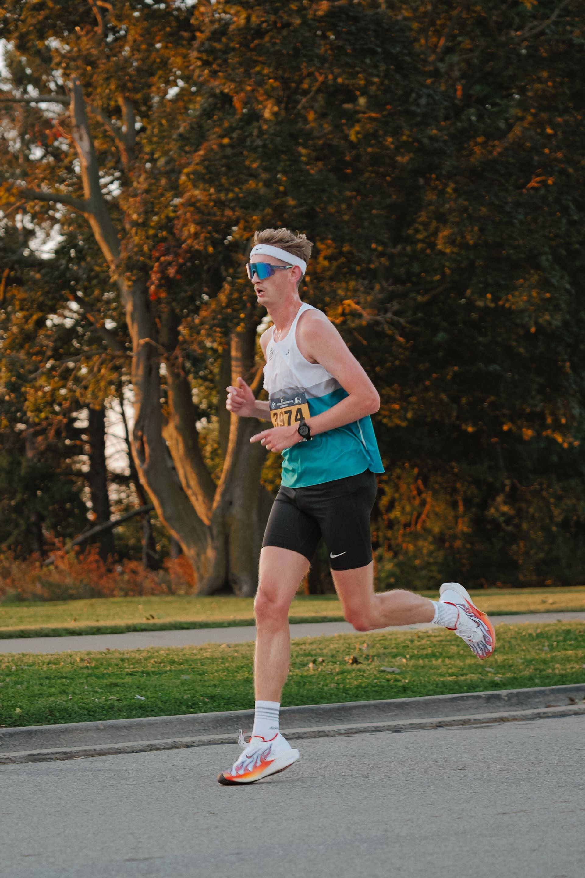 Runner in a blue tank top and black shorts jogging on a road near trees.