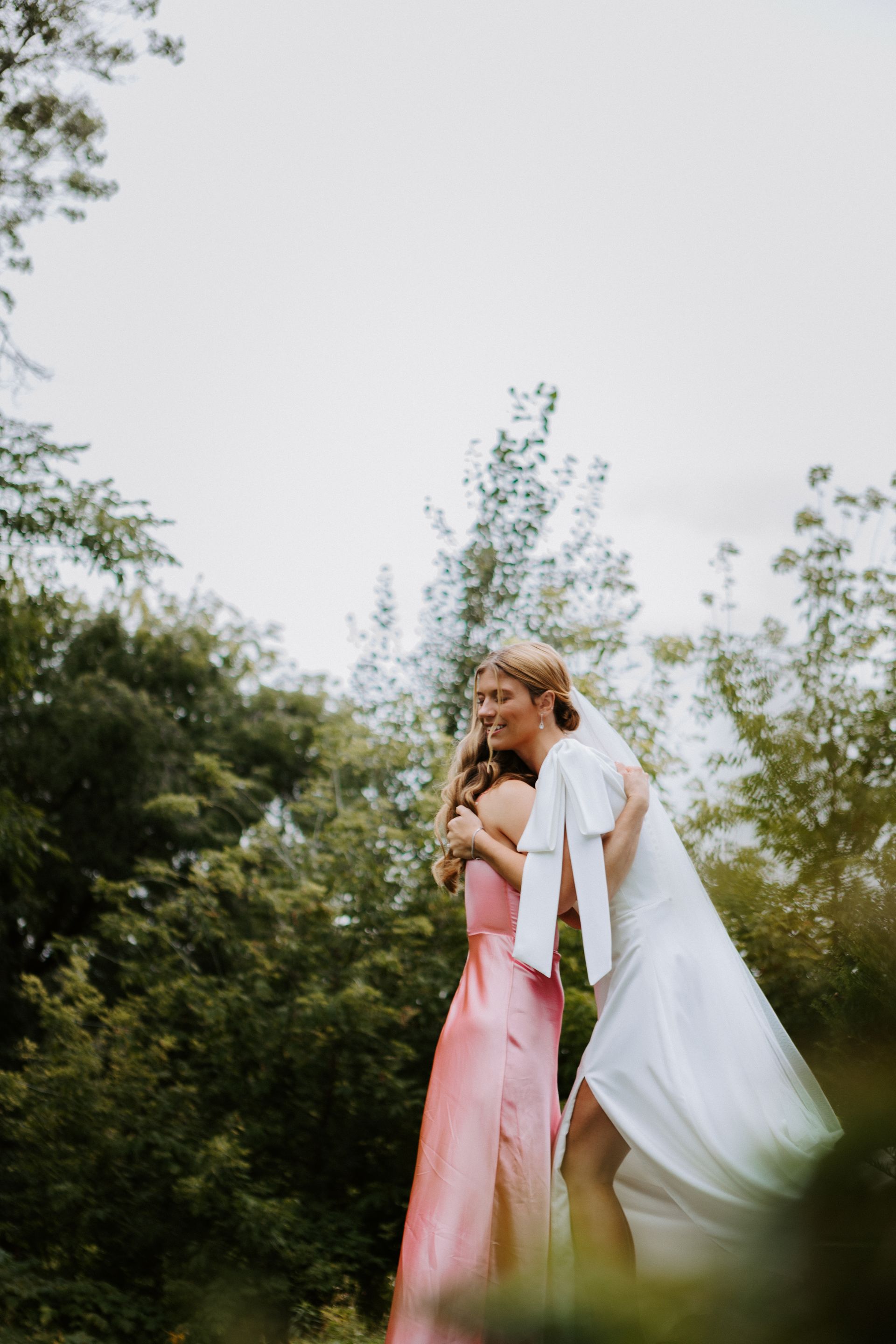 Couple embracing outdoors in wedding attire, bride in white dress and veil, groom in pink suit