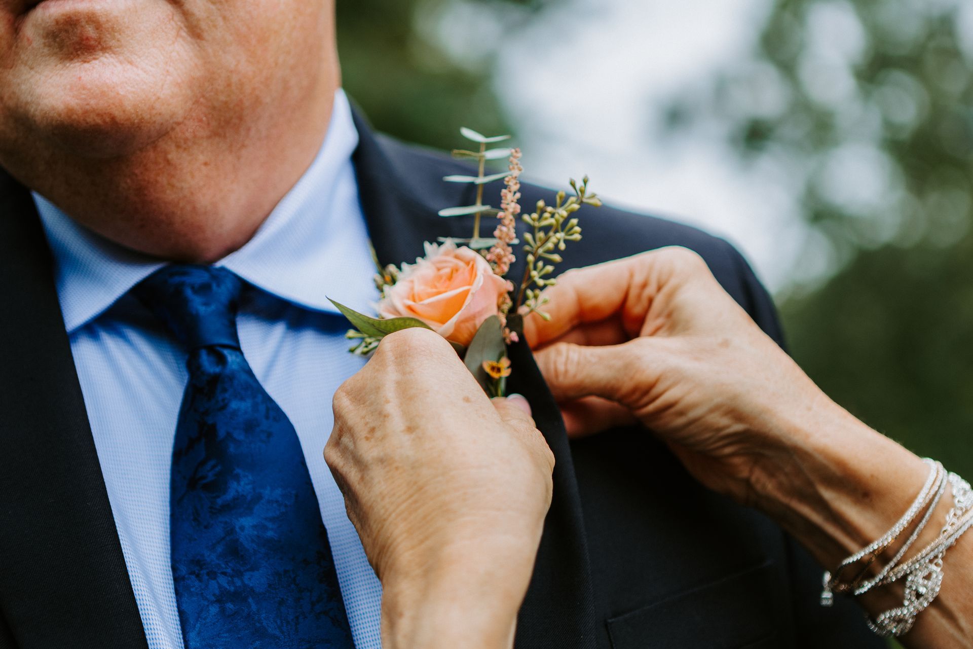 Hands pin a pink boutonniere onto a navy suit jacket
