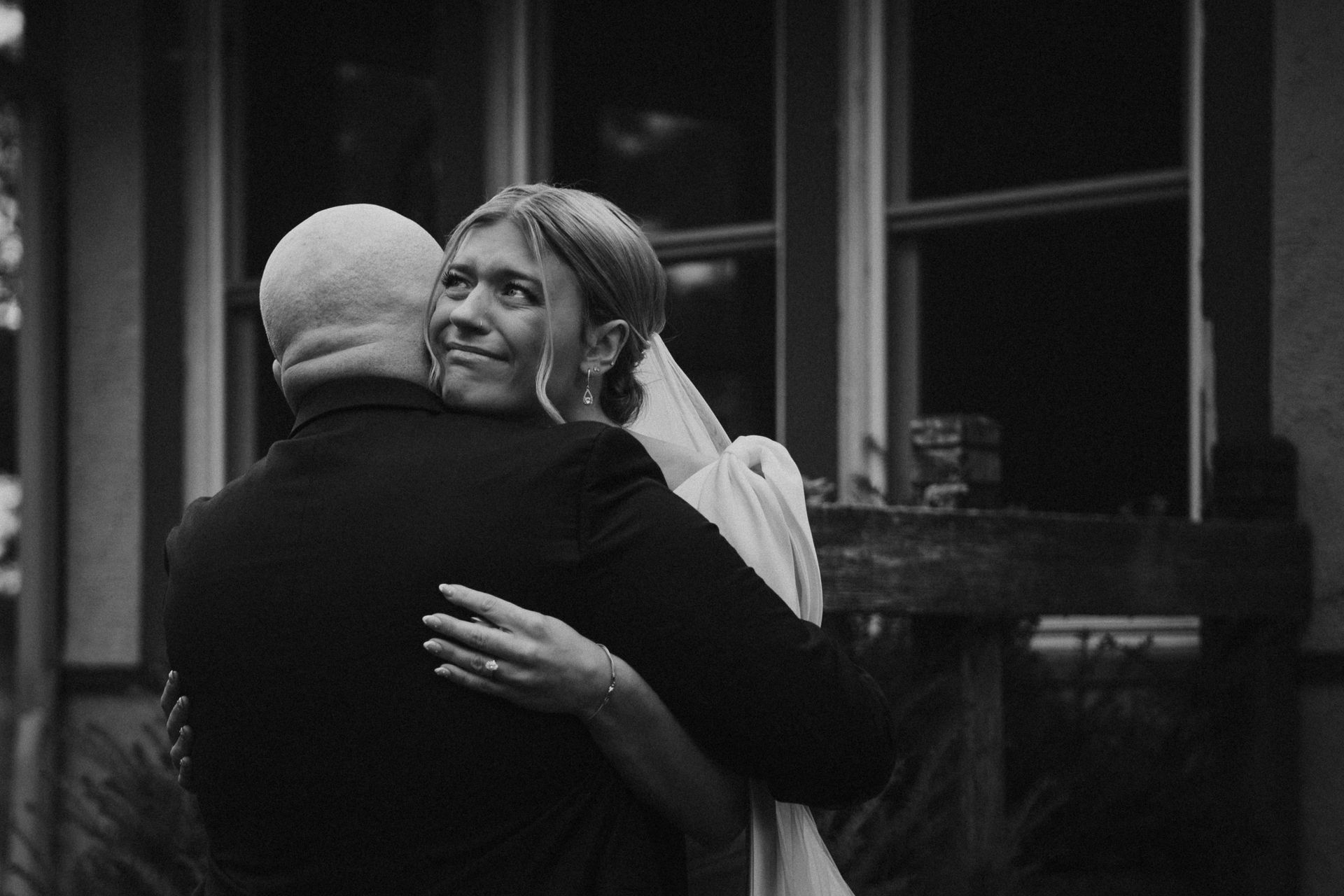 Two people embracing indoors, with one smiling and looking upward near a window.