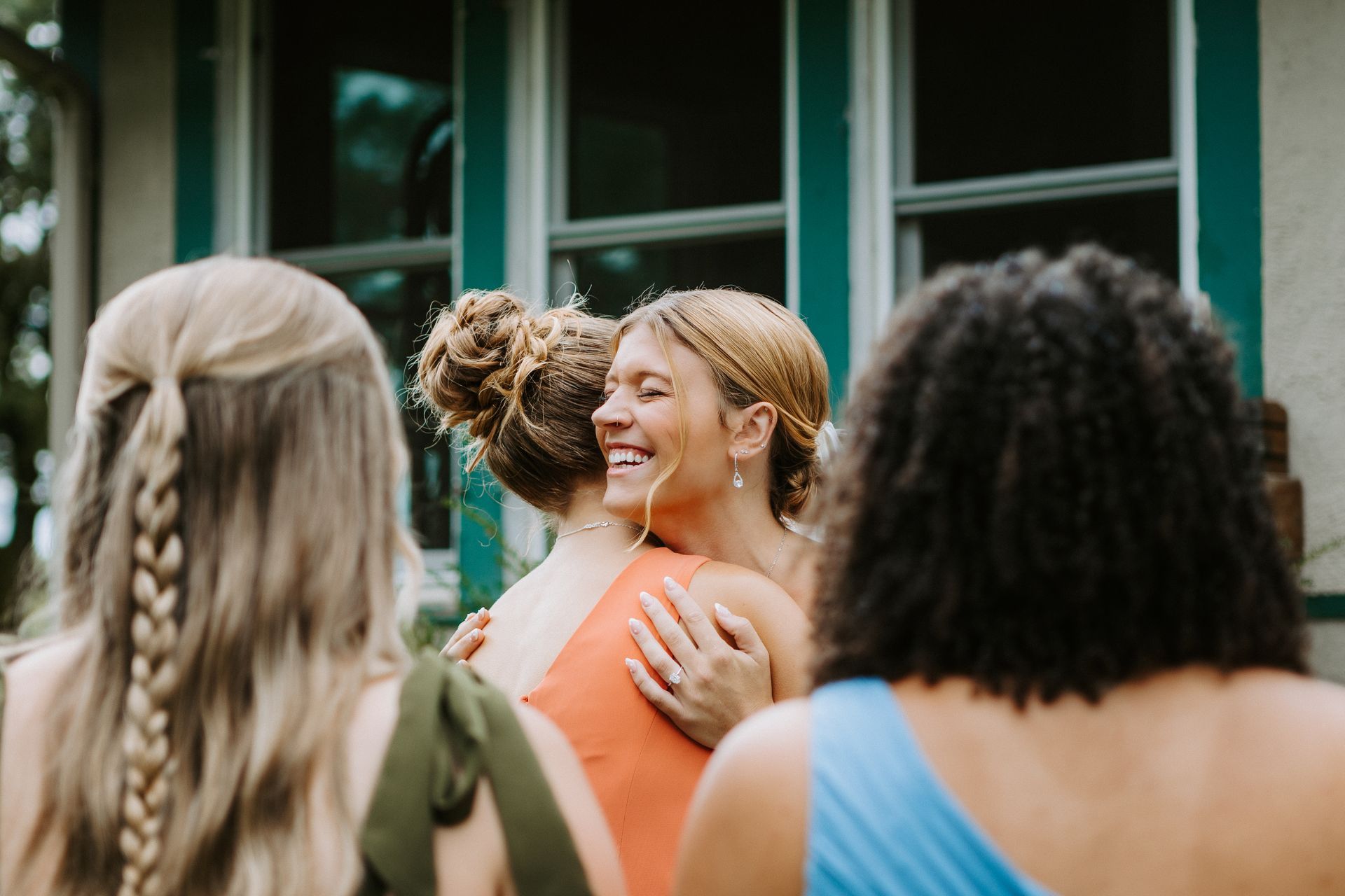 Friends hugging and smiling outdoors in front of a green house