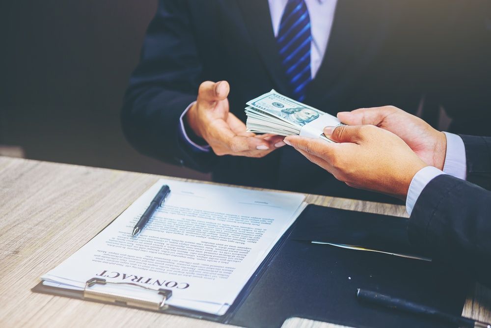 Businessperson handing cash across a desk with a contract and pen nearby