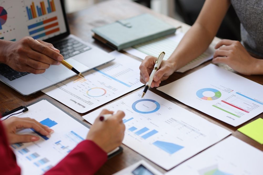 Hands reviewing business charts and graphs on papers around a conference table